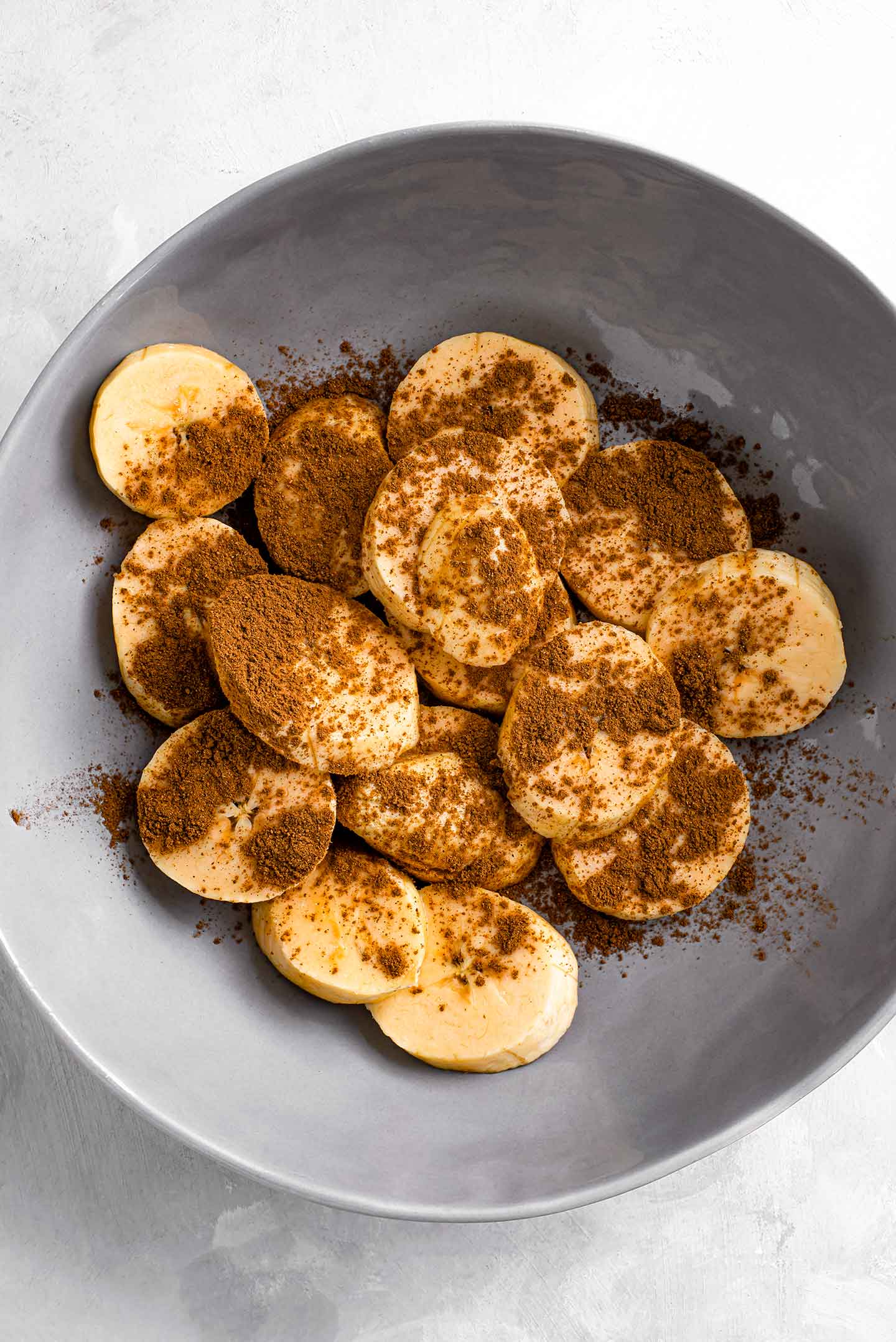 Top down view of ripe plantain slices in a shallow dish dusted with cinnamon and drizzled with maple syrup.