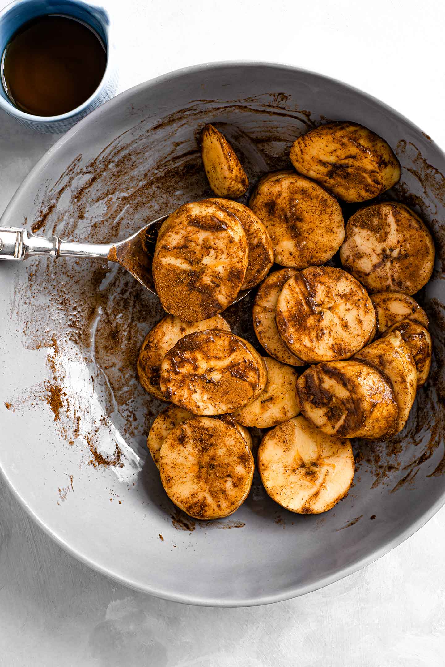 Top down view of plantain slices in a shallow dish being turned in cinnamon and maple syrup by a spoon.