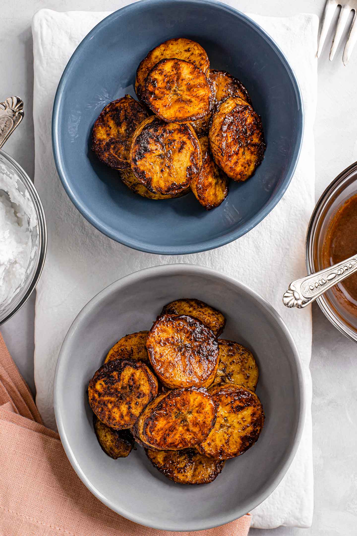 Top down view of golden caramelized plantain slices in two small bowls. The slices are golden and blackened around the edges.