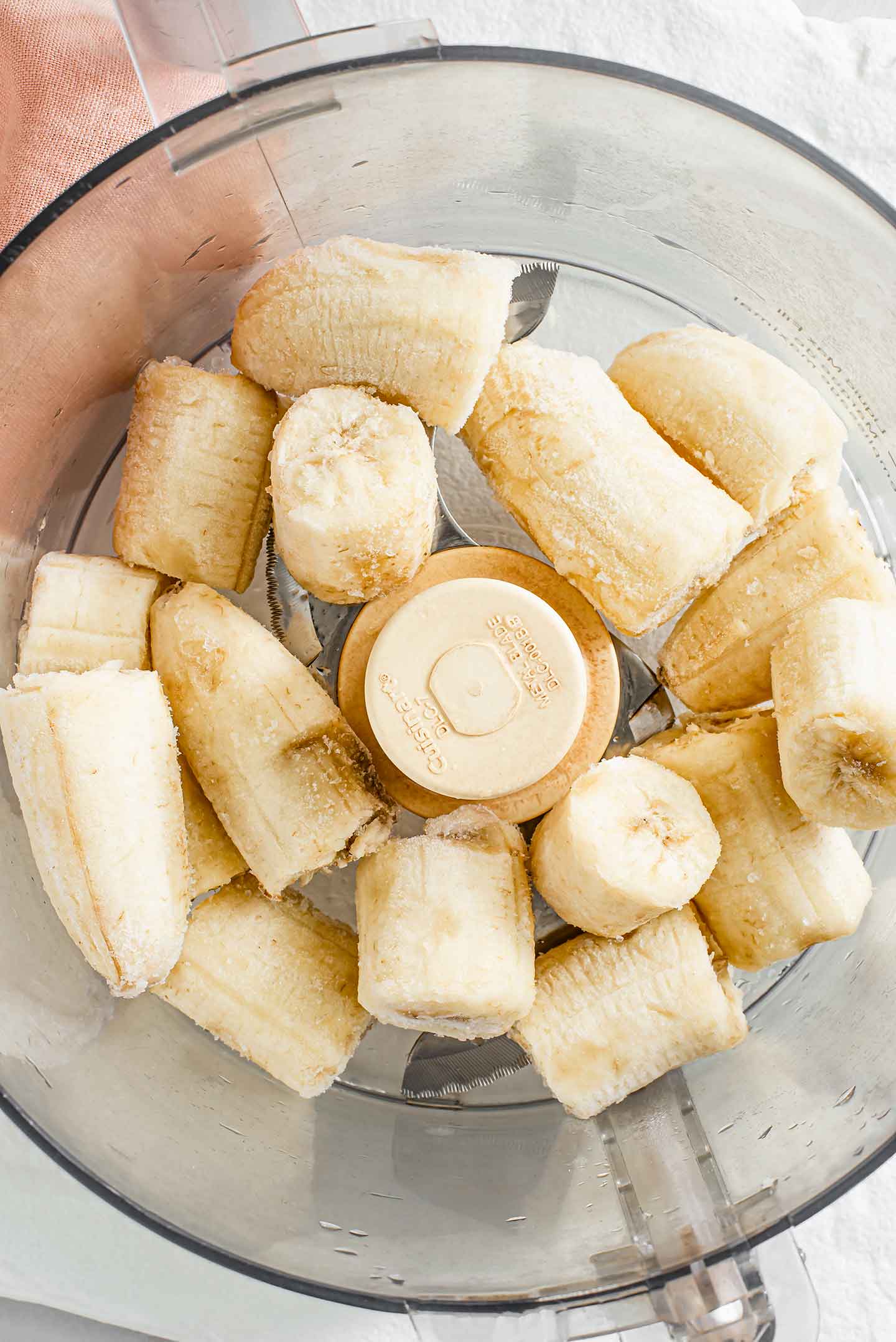 Top down view of frozen banana chunks in a food processor.