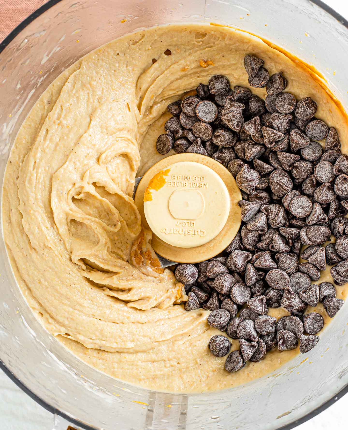 Top down view of chocolate chips added to a creamy banana, peanut butter nice cream in a food processor.