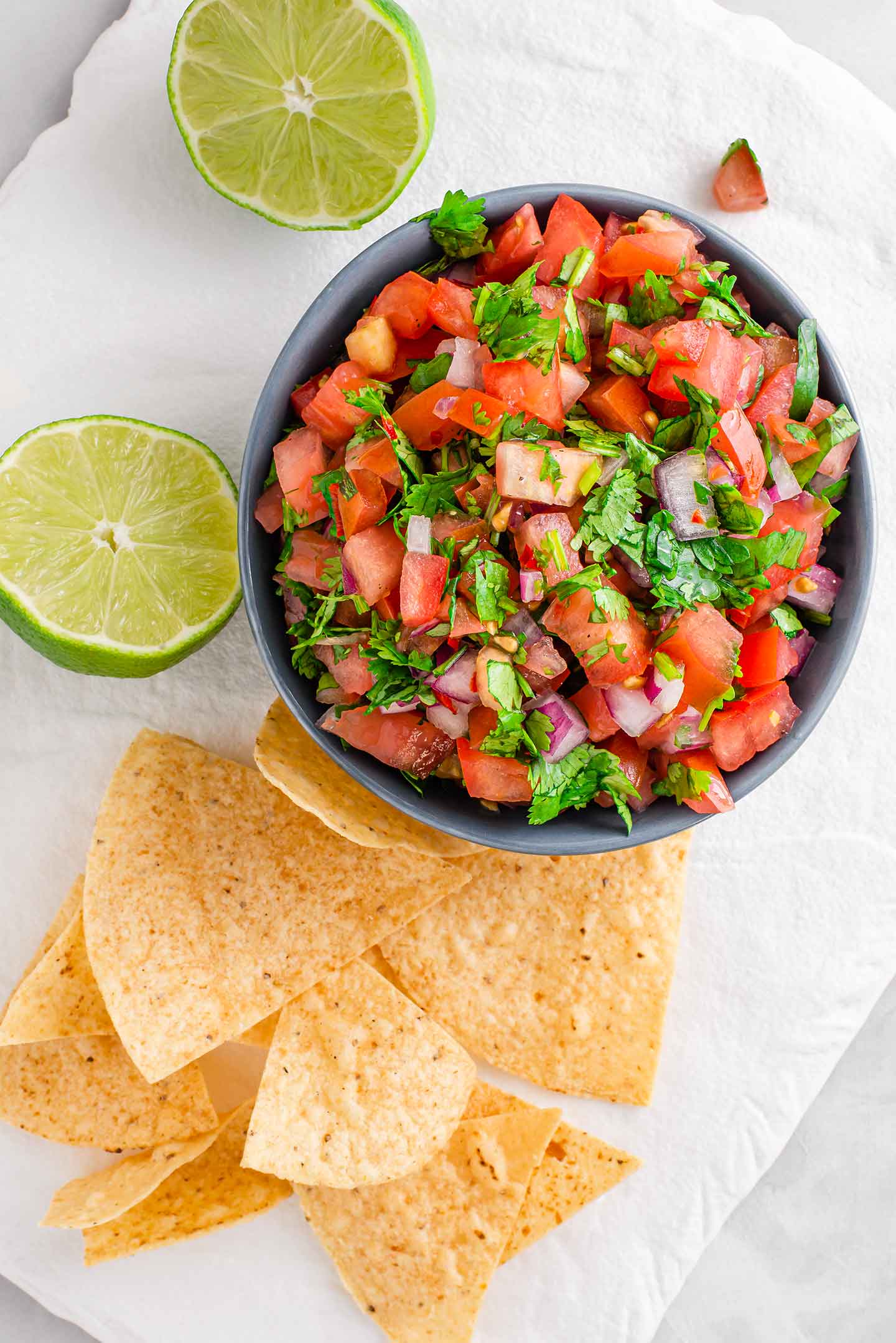 Top down view of easy homemade salsa fresca in a small dish with lime wedges and tortilla chips surrounding.