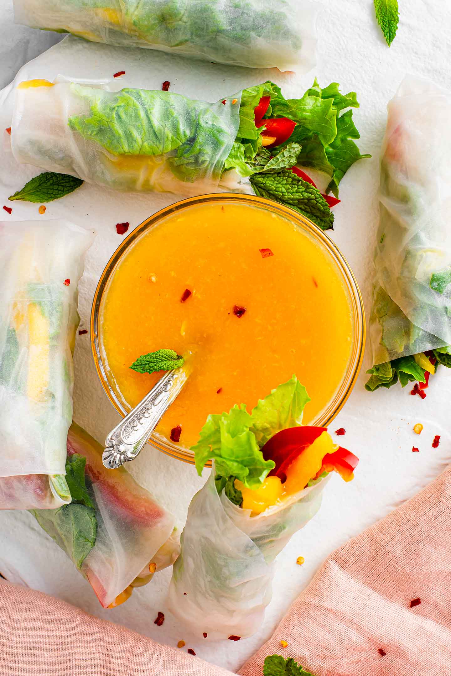Top down view of easy mango chilli sauce in a bowl with red pepper flakes garnishing the top. Surrounding the bow are fresh mango spring rolls.