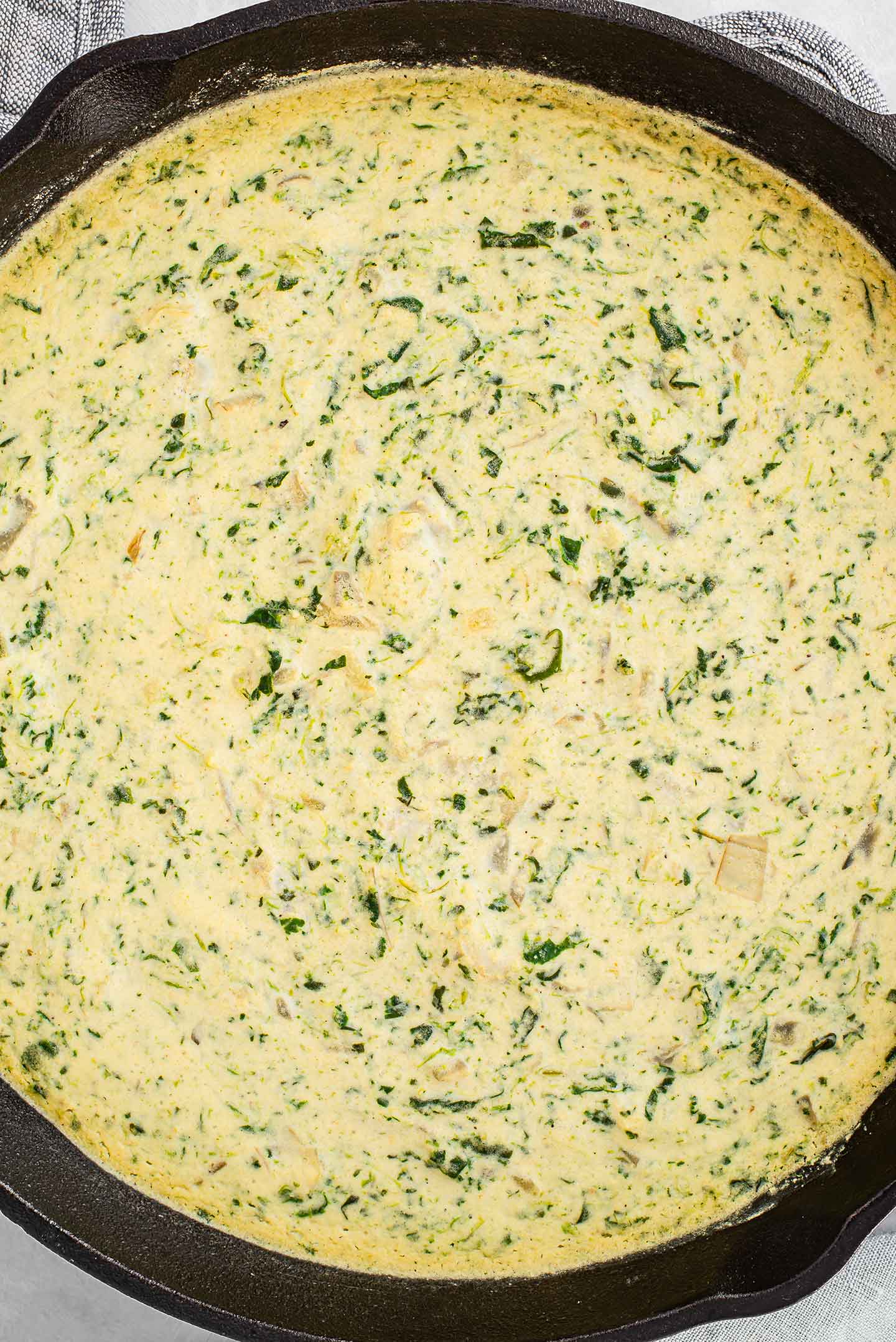 Top down view of a cast iron skillet filled with spinach white bean dip. The dip is lightly browned on top and warm from the oven.