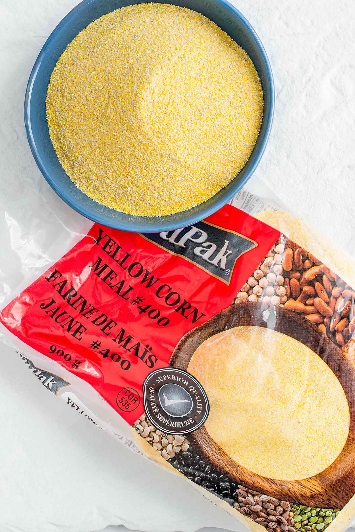 Top down view of raw polenta, or cornmeal, in a small dish with the packaging for the fine grain yellow corn meal beside it.