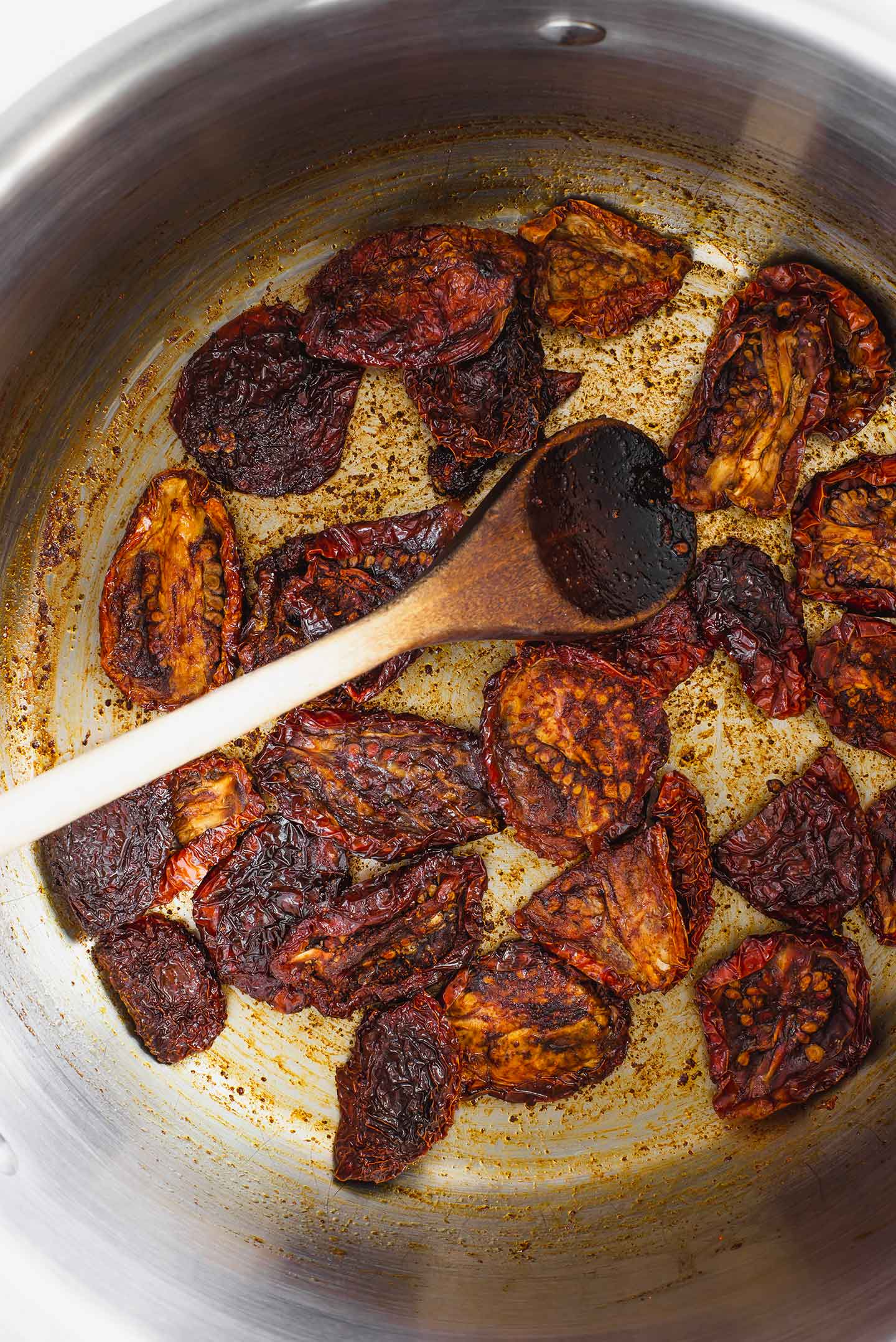 Top down view of sun-dried tomatoes in a large pot. They are browned and seasoned with tamari, liquid smoke, and smoked paprika.