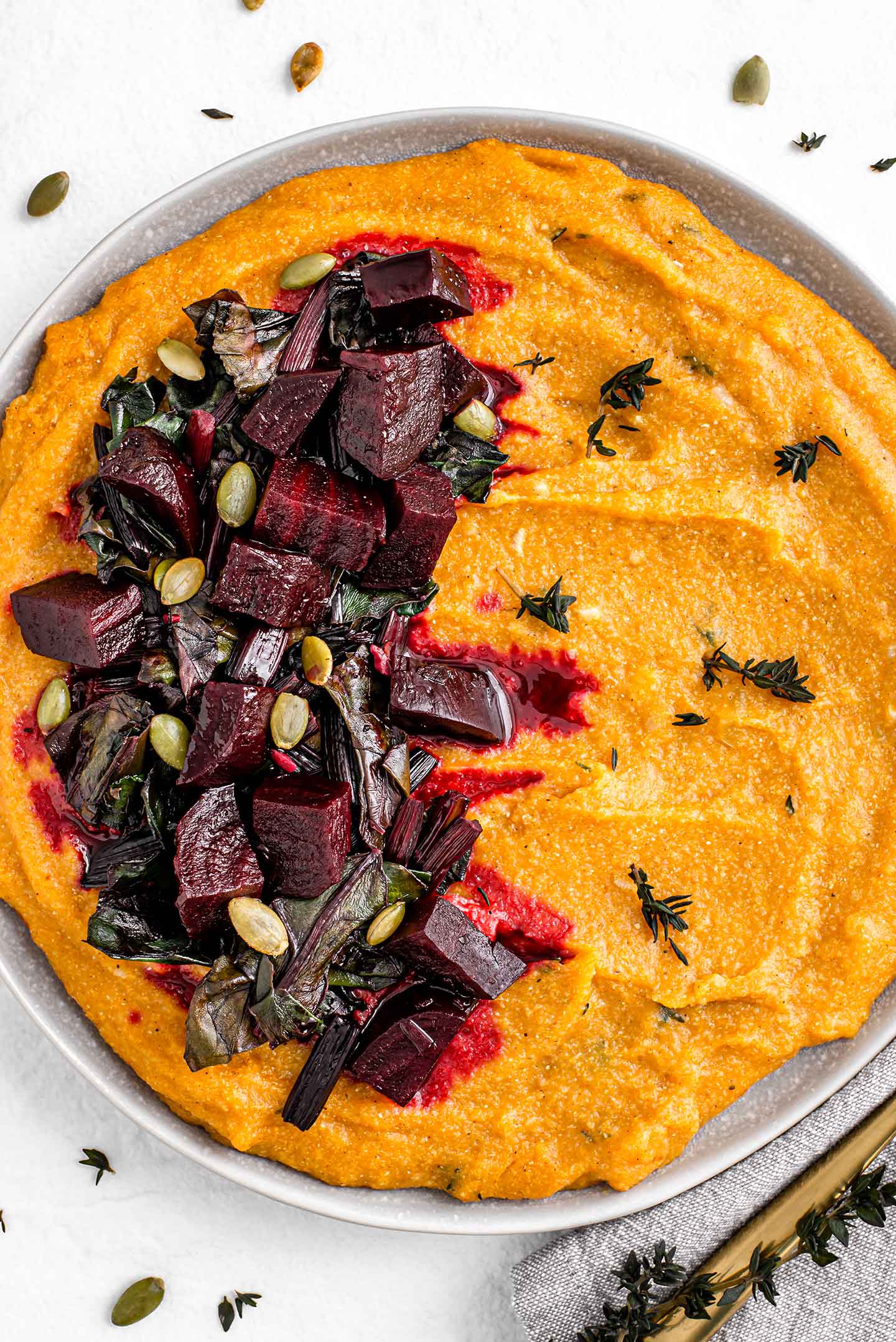 Top down view of pumpkin beet polenta filling a dish. Roasted beets and sauteed beet greens sit atop the orange coloured polenta. Fresh thyme garnishes the dish.