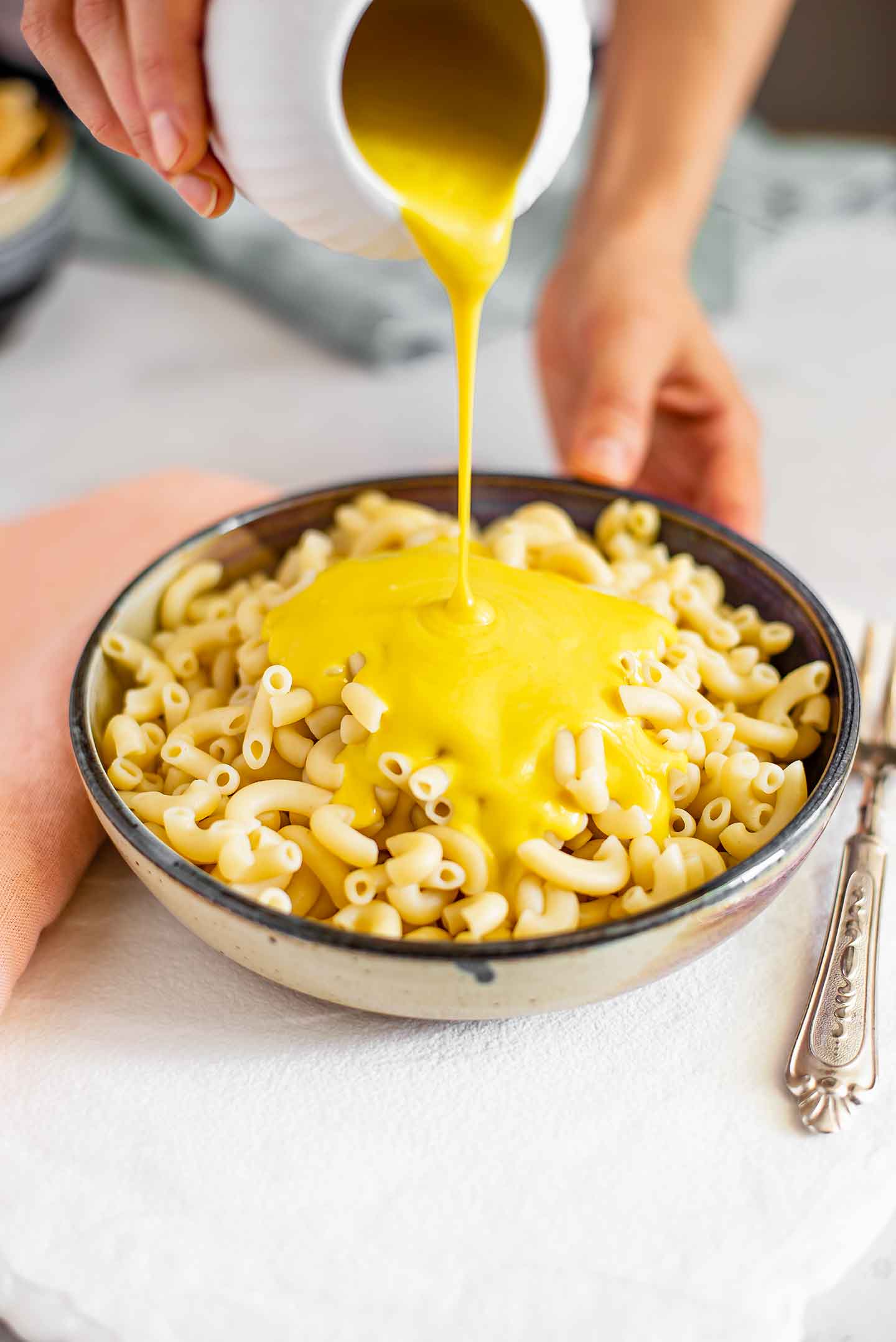 Side view of yellow queso mac and cheese sauce being poured over a bowl of macaroni noodles.