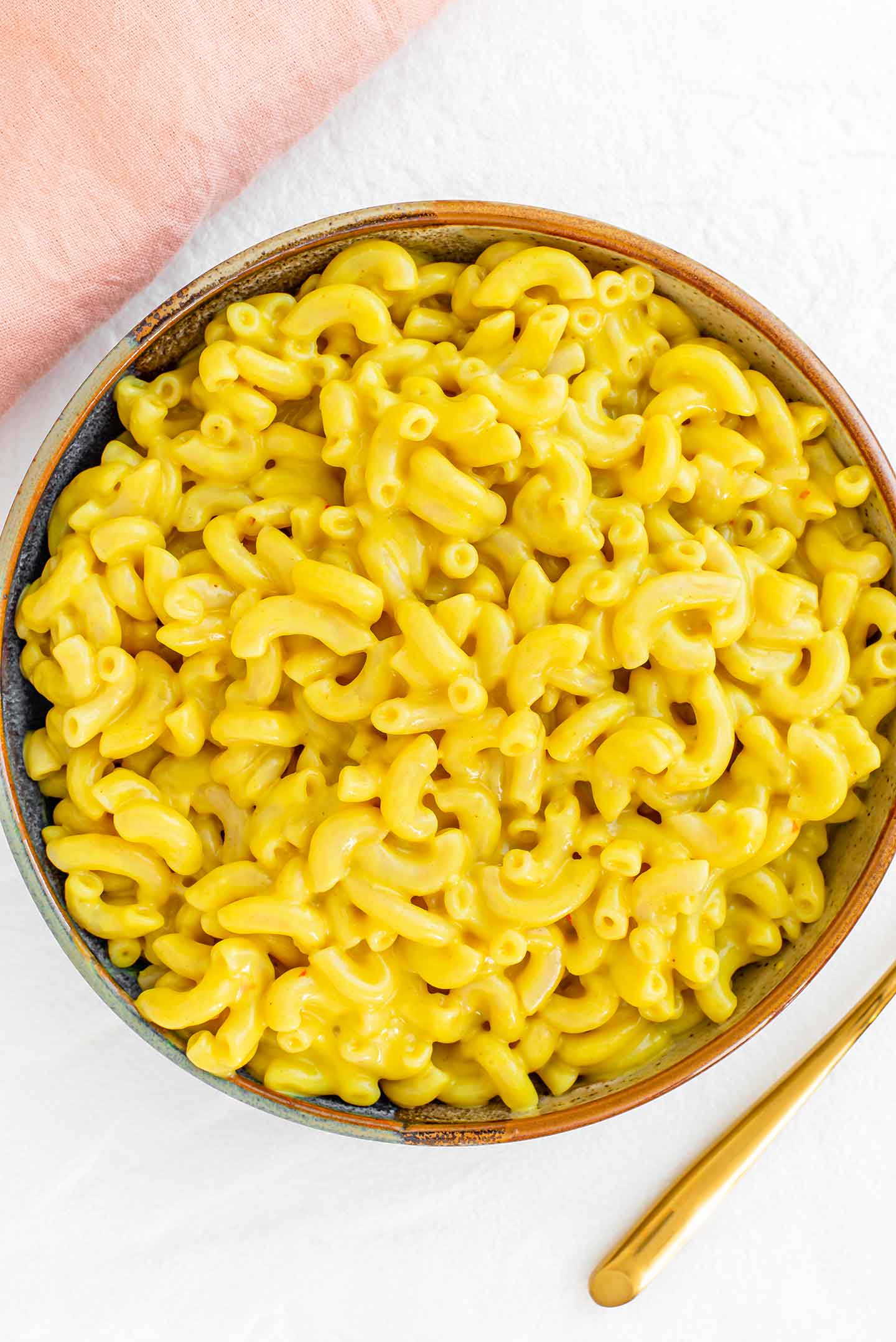 Top down view of a bowl full of yellow macaroni noodles. The noodles are covered in the creamy, "cheesy", queso mac and cheese sauce.