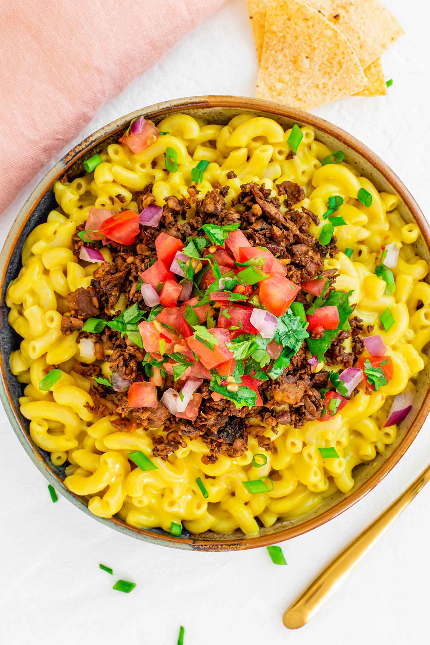 Top down view of a bright yellow bowl of queso mac and cheese topped with walnut, mushroom ground round, and salsa fresca.