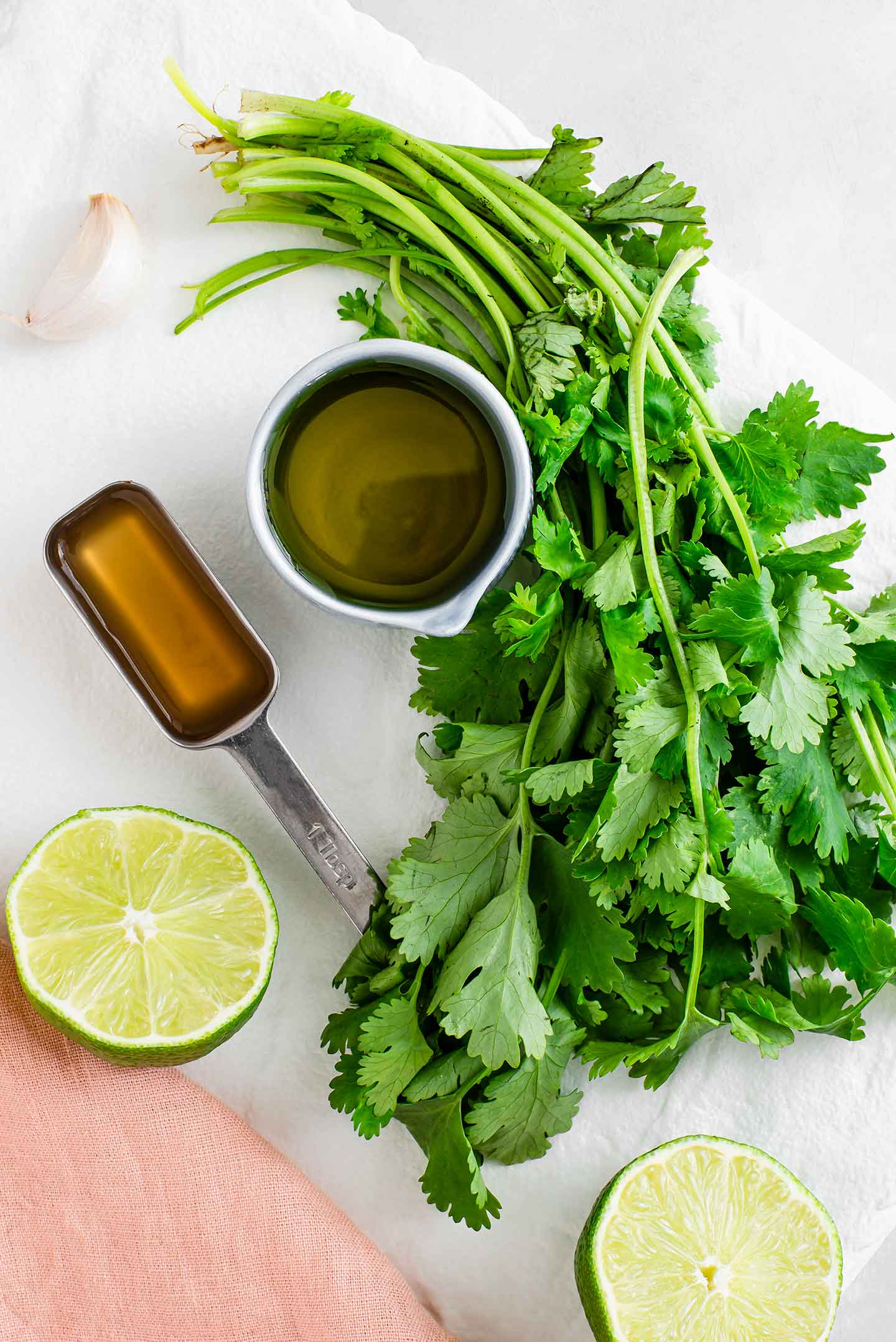 Top down view of cilantro, a sliced lime, a clove of garlic, a tablespoon of apple cider vinegar and a small dish of olive oil on a white tray.
