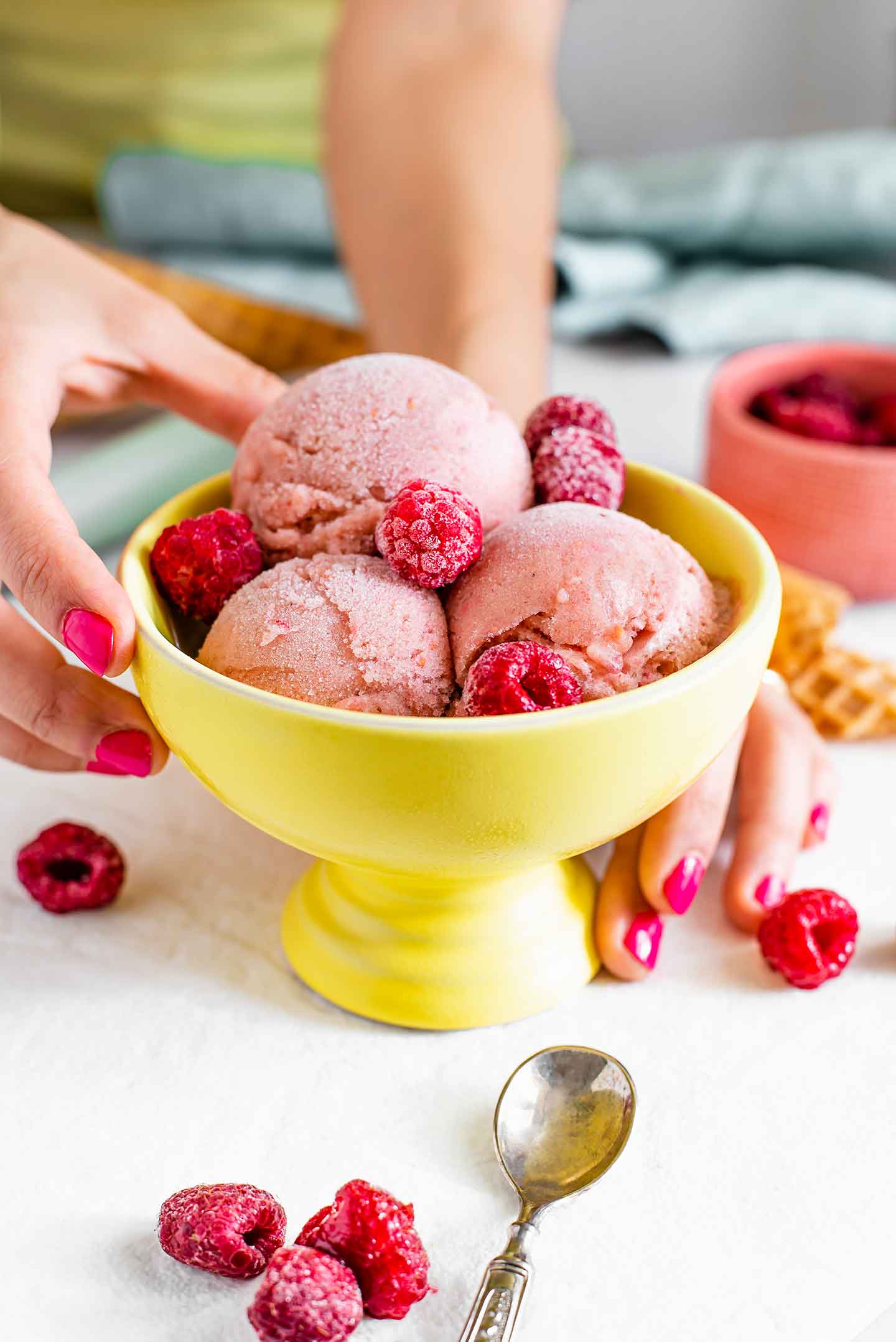 Side view of three scoops of raspberry nice cream garnished with frozen raspberries in a bright yellow sorbet bowl.