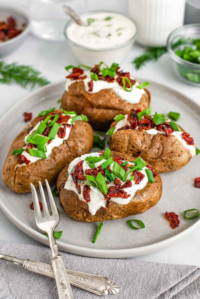 Top down view of 4 simple baked potatoes loaded with sour cream, sun-dried tomato bits, and sliced green onion.