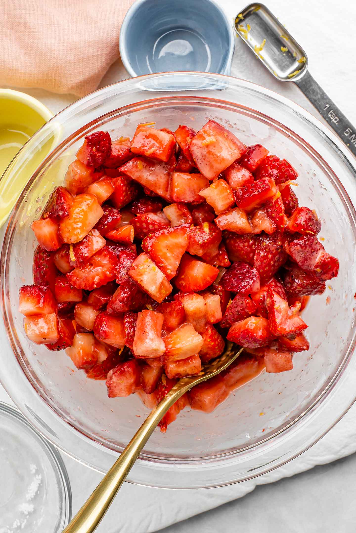 Top down view of diced strawberries with a thicker sauce on them. Pieces of lemon zest are visible on the berries and they have been coated in sugar and starch.