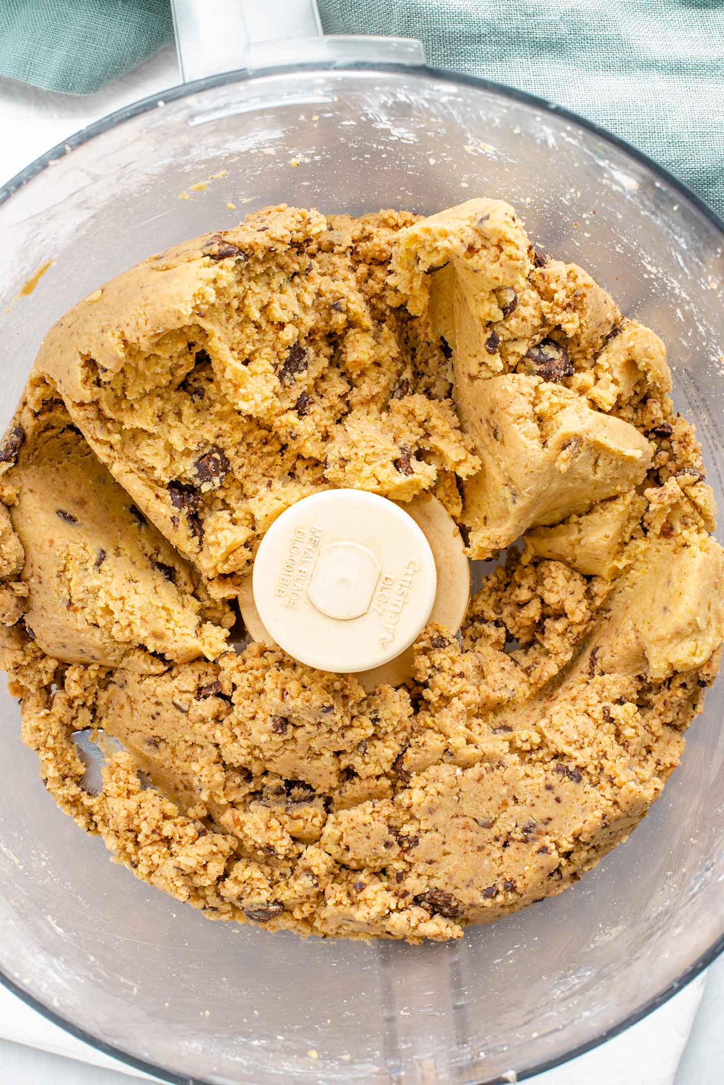 Top down view of the finished dough in a food processor. The dough is firm in texture and speckled with chocolate chips.