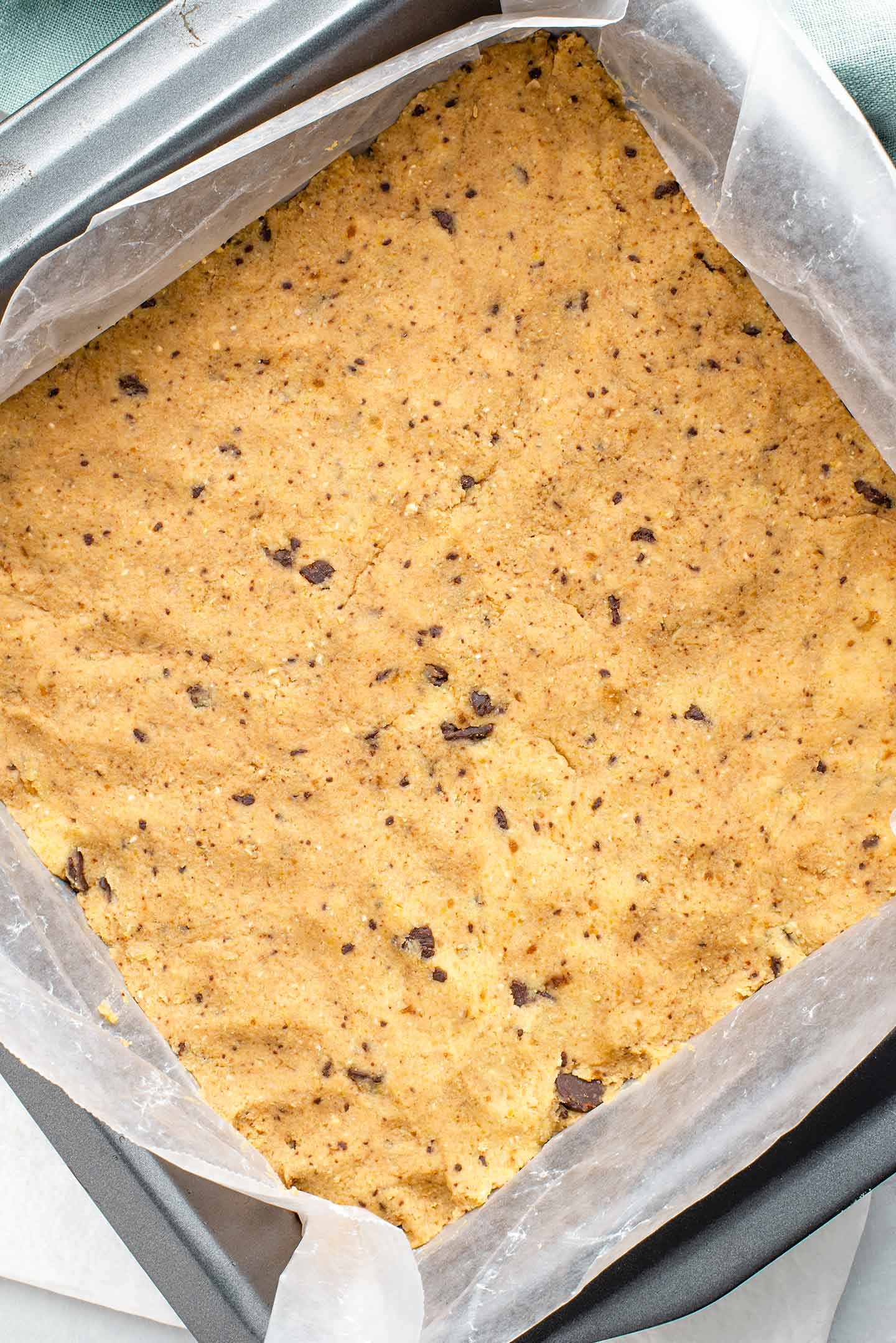 Top down view of the cookie dough base pressed into a baking tin lined with wax paper.