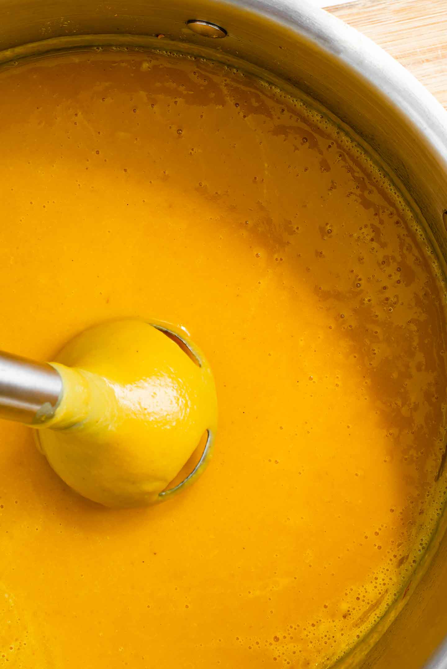 An immersion blender pulls up from a creamy, blended, butternut squash soup.