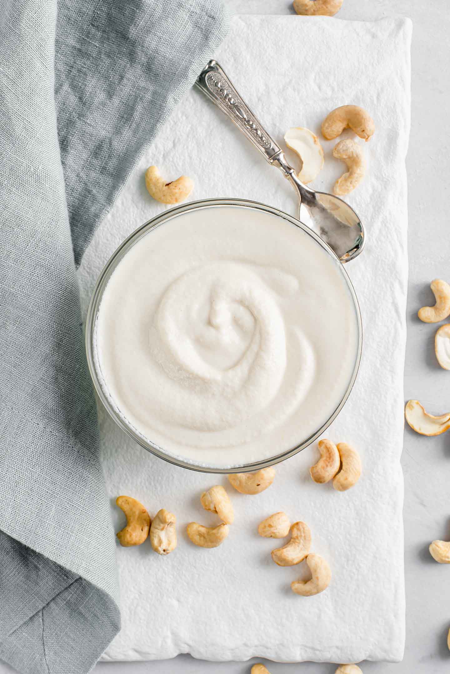 Top down view of 4 Ingredient sour cream in a small glass dish. The cream is thick with a swirl through it. Cashews are scattered on a white tray around the dish.