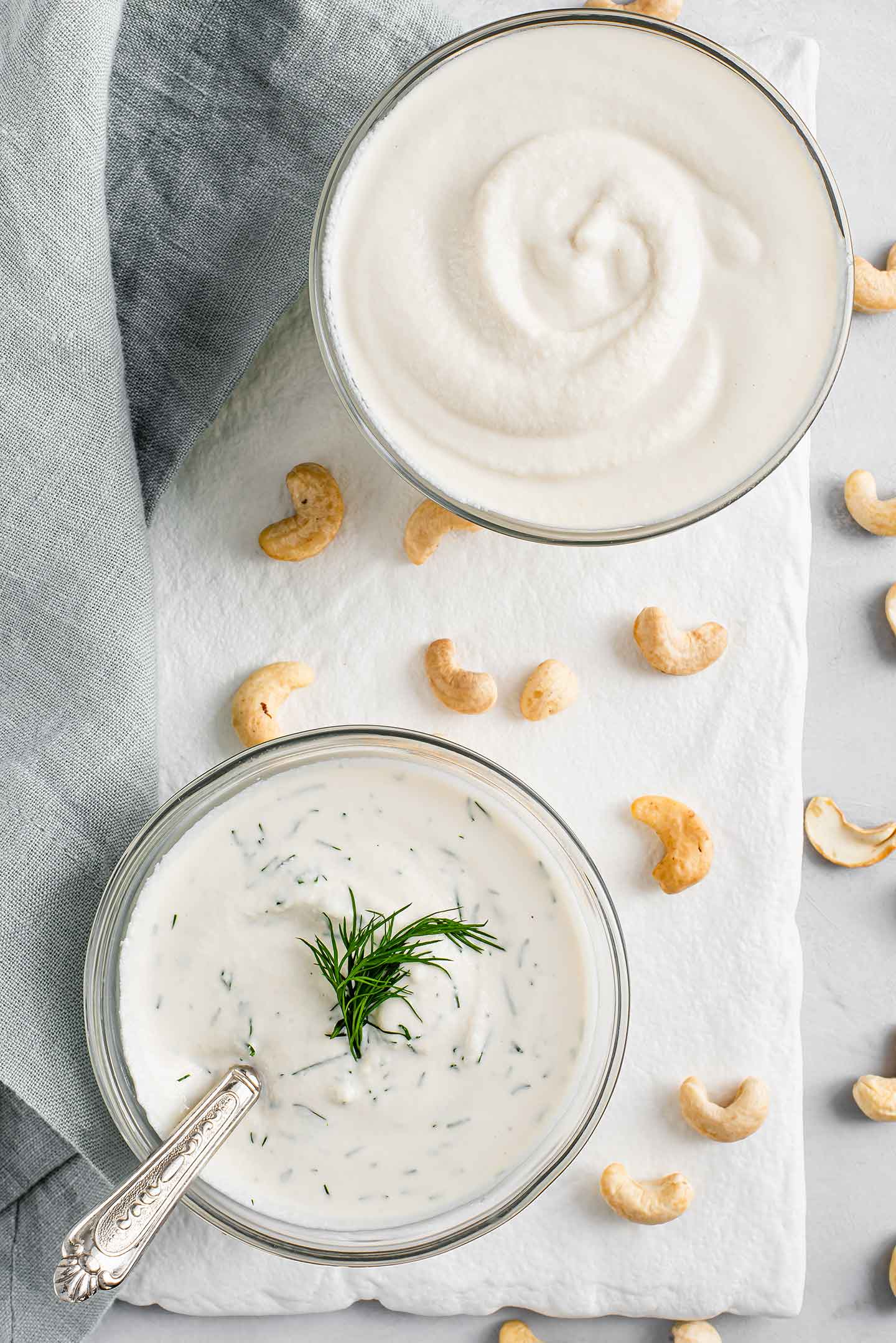 Top down view of plain sour cream and dill infused sour cream. The dill sour cream has a fresh sprig of dill on top and cashews are scattered between the two bowls.