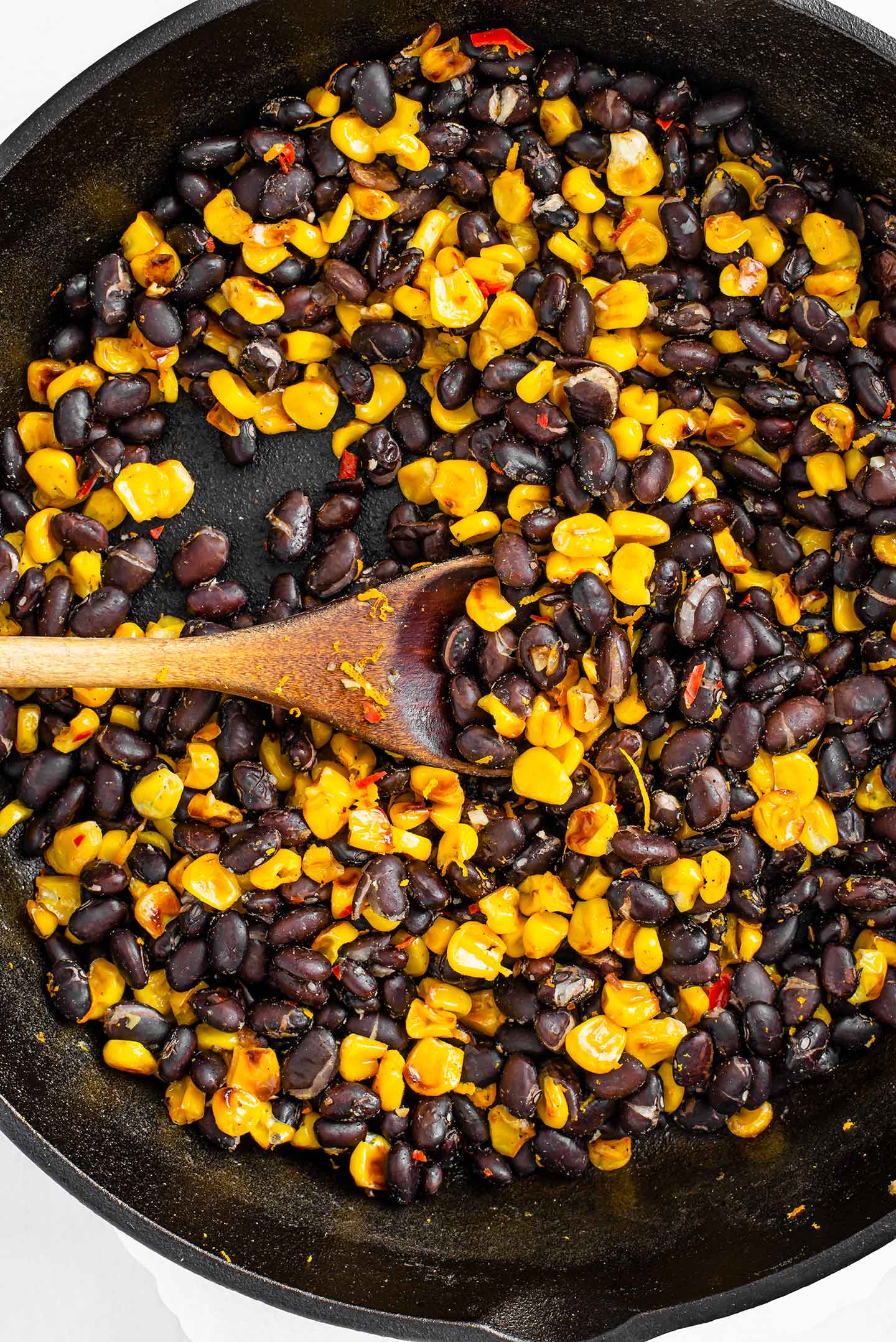 Top down view of corn and black beans in a cast iron skillet. Pieces of red chilli pepper are visible, the corn is nicely browned, and the beans have dried and split open.