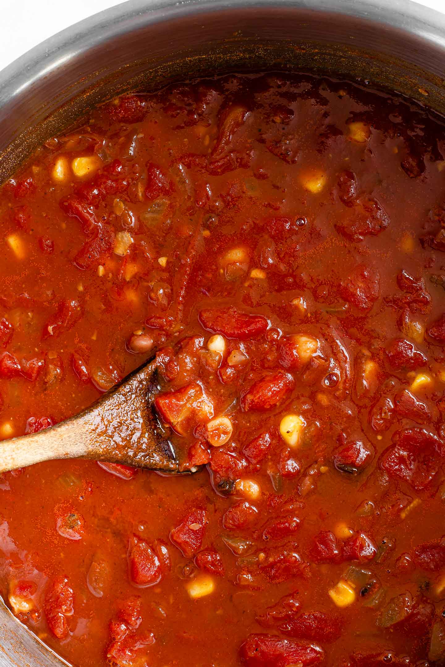 Top down view of a wooden spoon stirring the chunky chilli in a large pot.