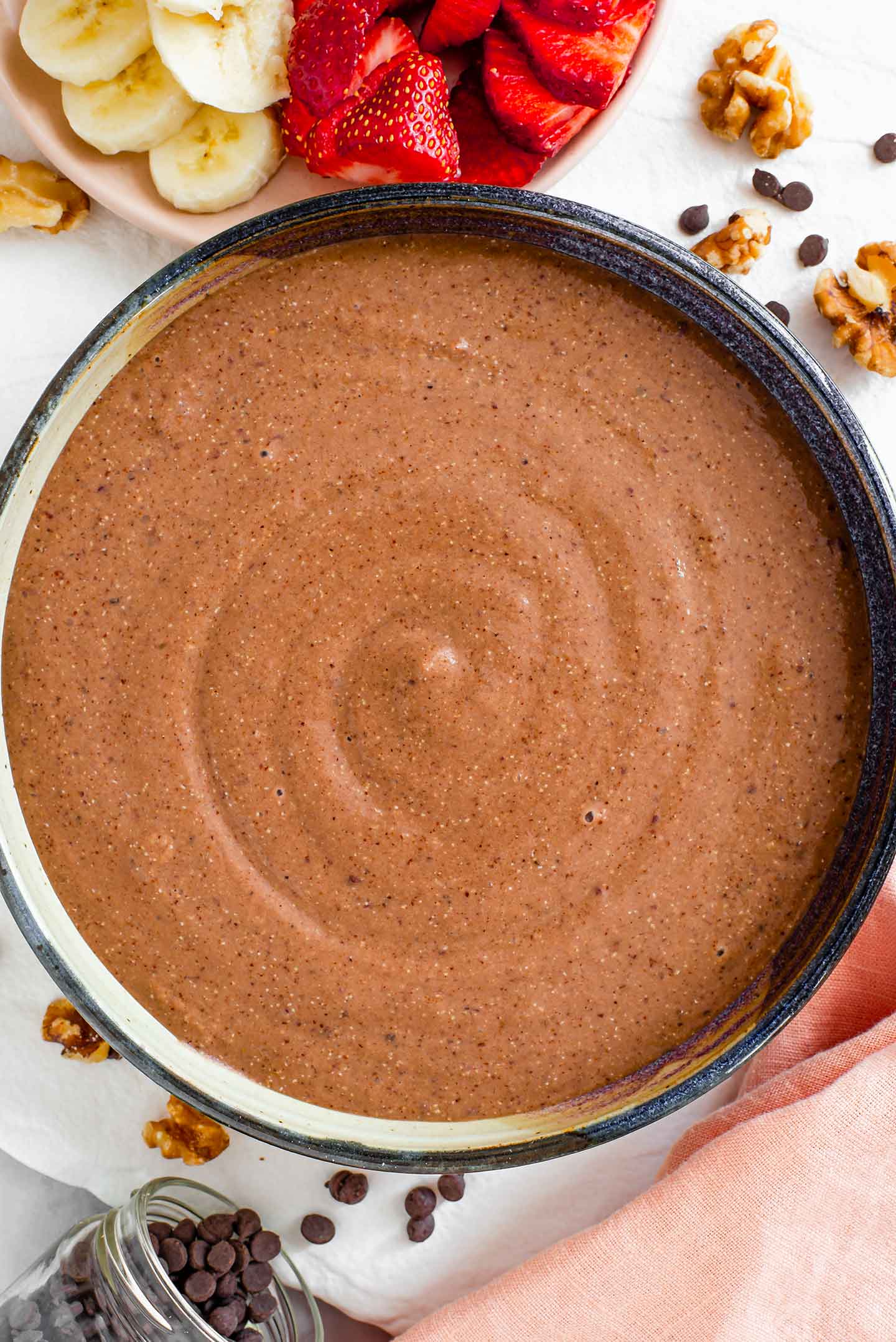 Top down view of a chocolate smoothie swirled in a wide shallow bowl. The smoothie is lightly speckled with the fine texture of blended quinoa.