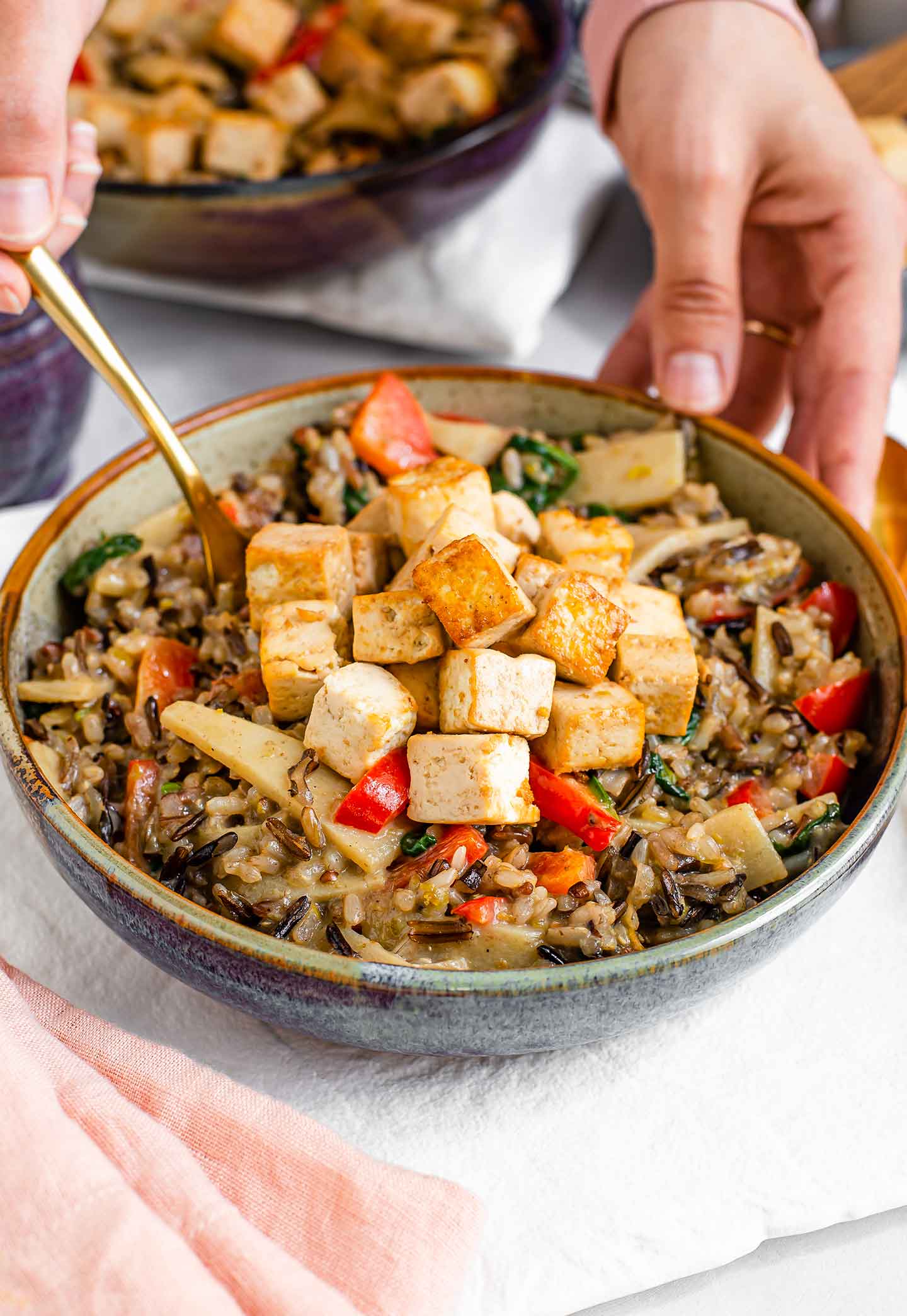 Side view of a hand dipping a fork into the creamy fried rice and crispy tofu. 