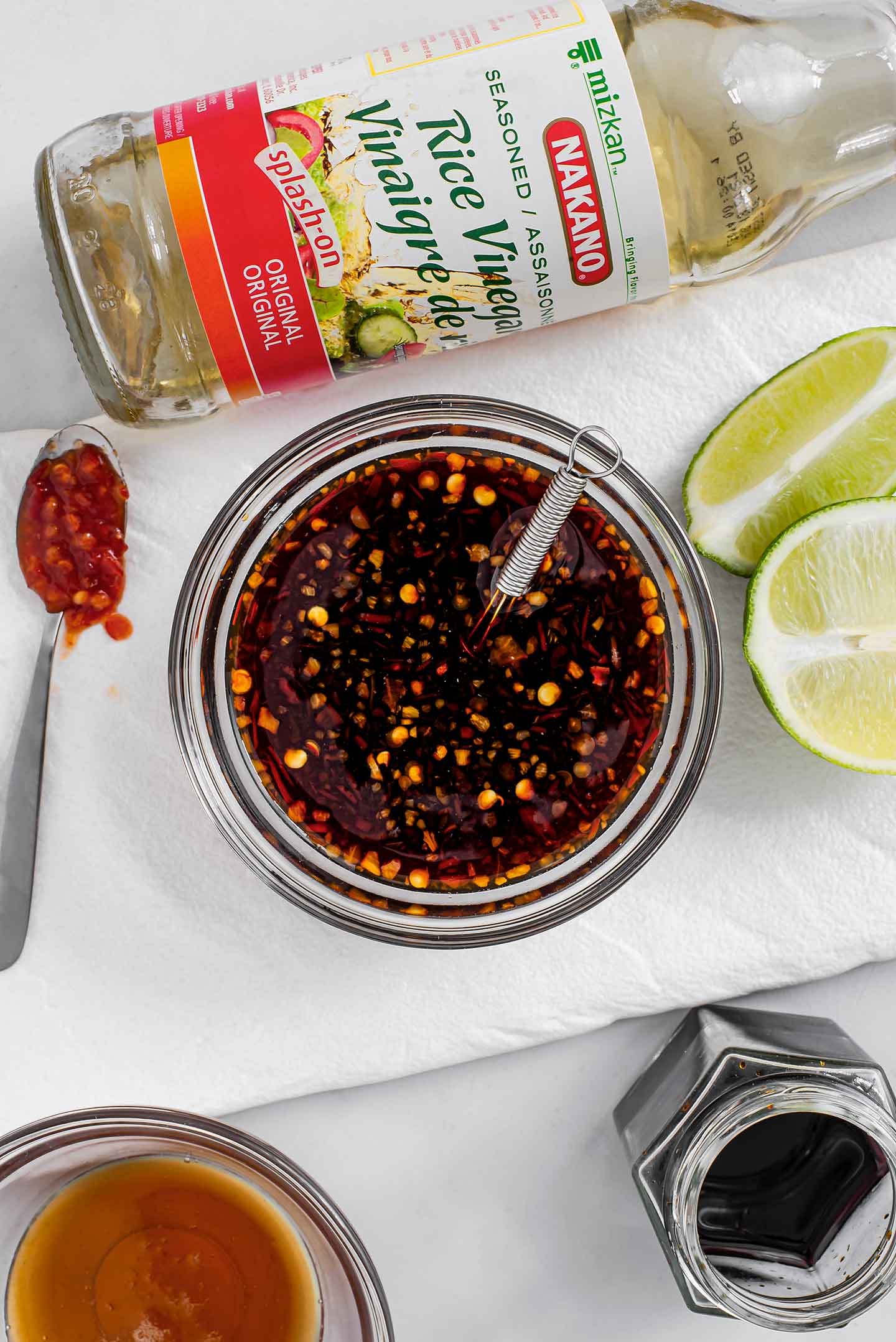 Top down view of pad thai sauce in a small dish with rice vinegar, lime wedges, chilli garlic sauce, tamari, and maple syrup scattered around.