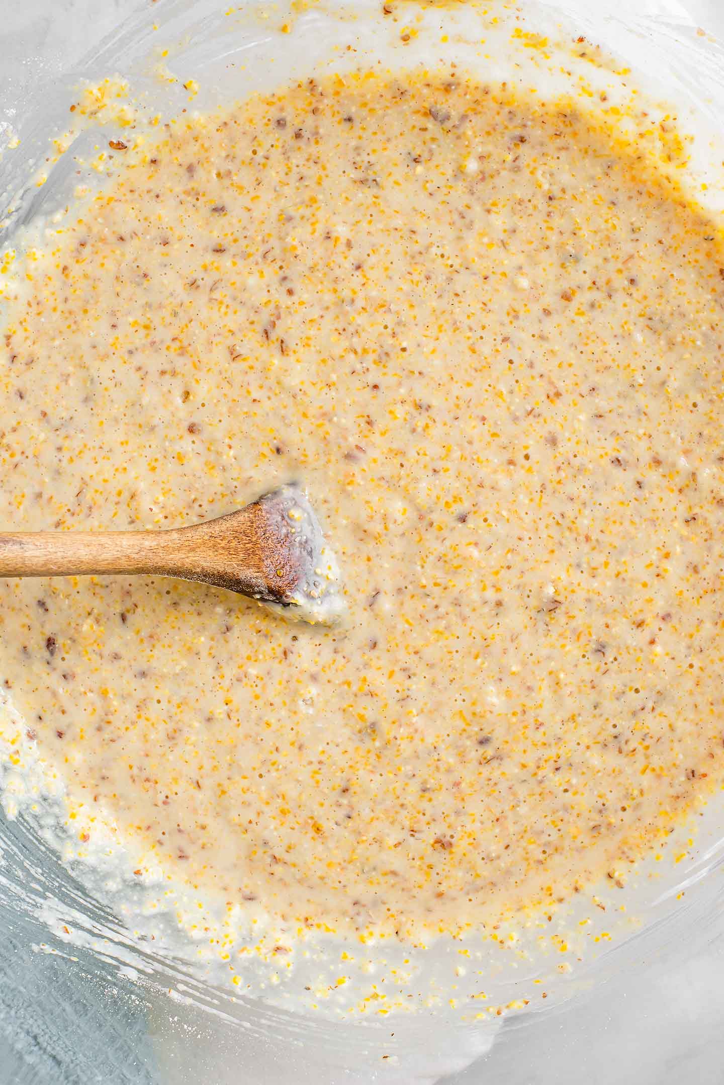Top down view of cornbread batter being mixed in a large glass bowl.