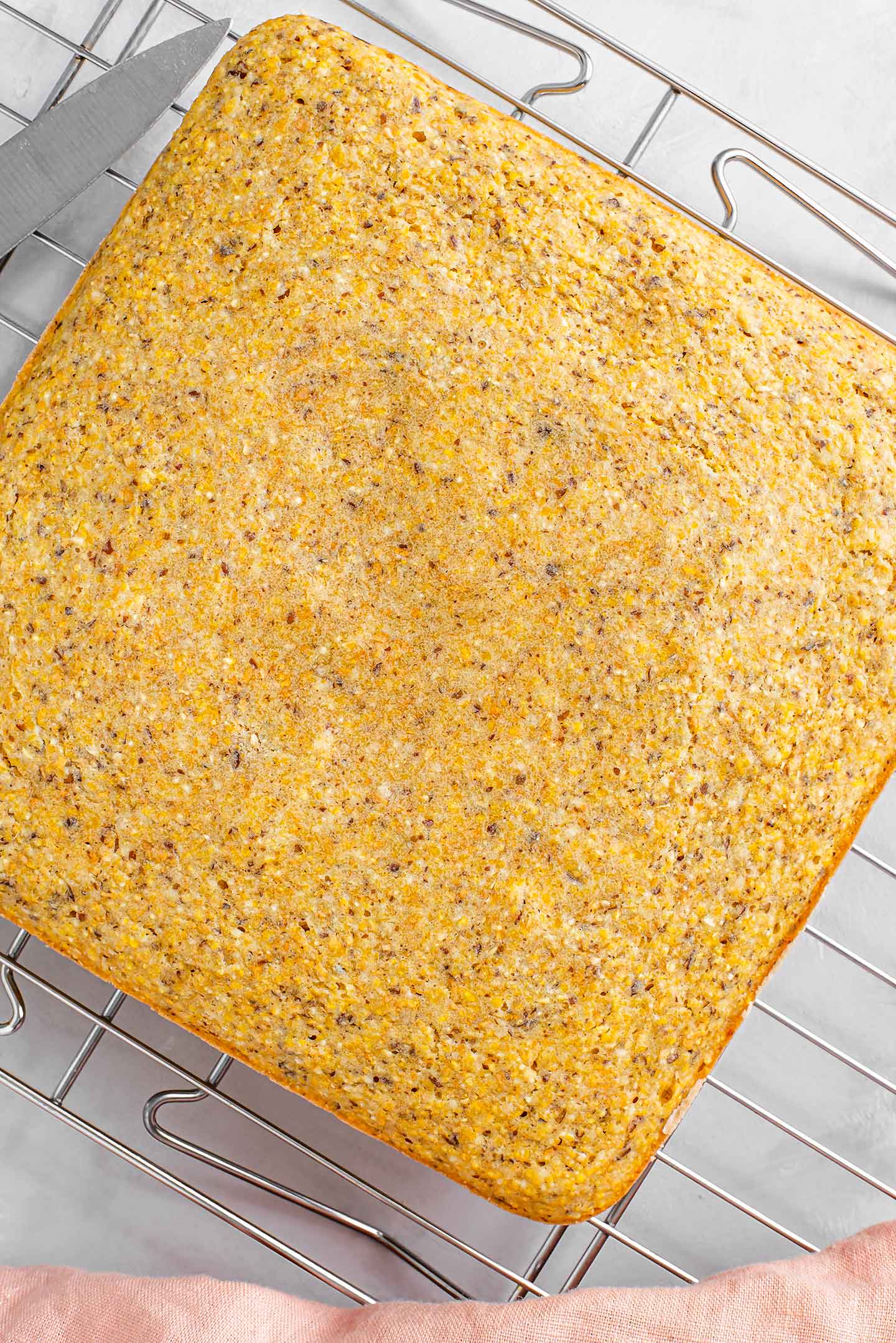 Top down view of a baked, golden square loaf of cornbread cooling on a wire rack.