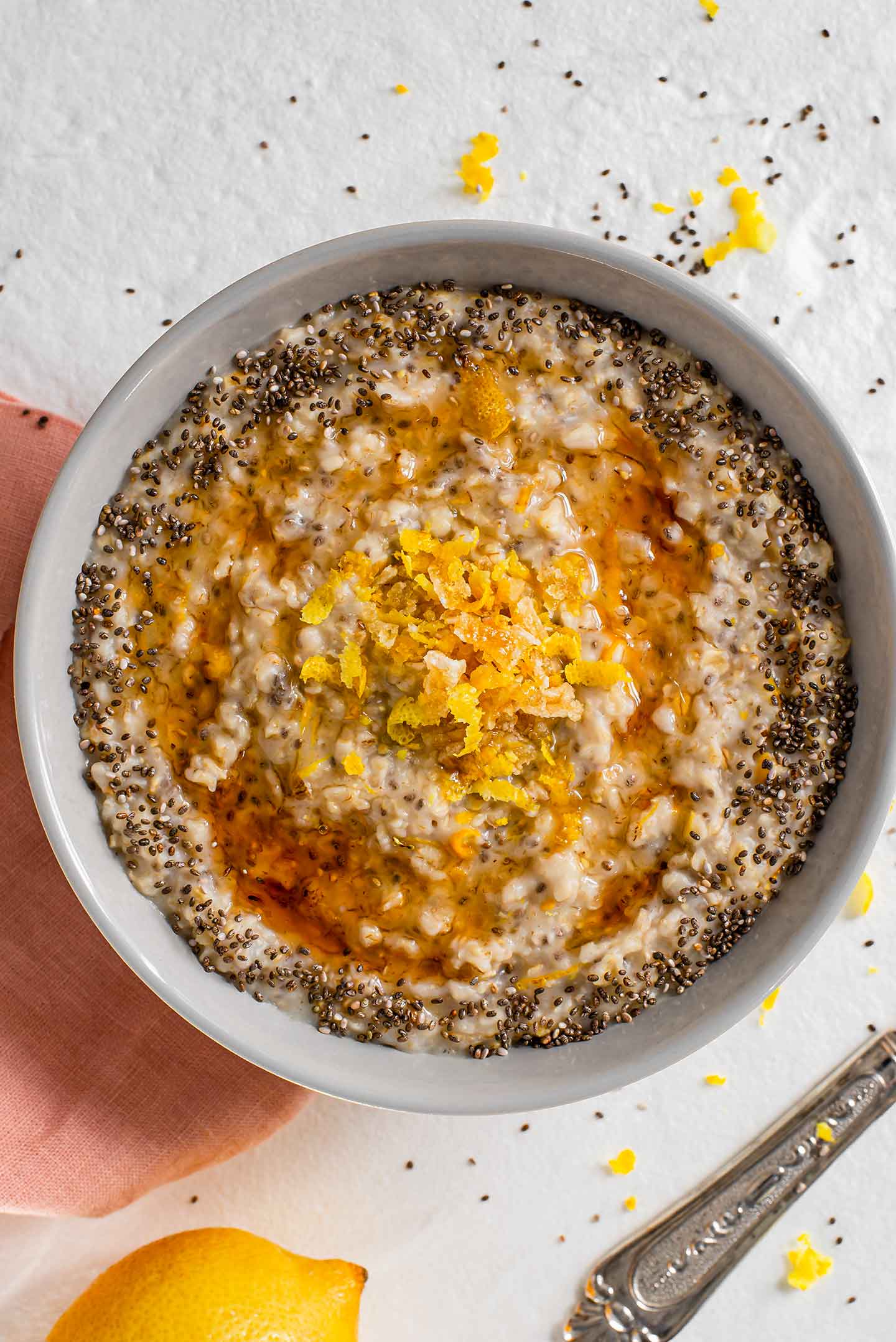 Top down view of maple syrup swirled in a bowl of lemon chia oats. Extra chia seeds are sprinkled in a ring around the perimeter of the oats. Candied ginger and lemon zest are piled in the centre of the oats.