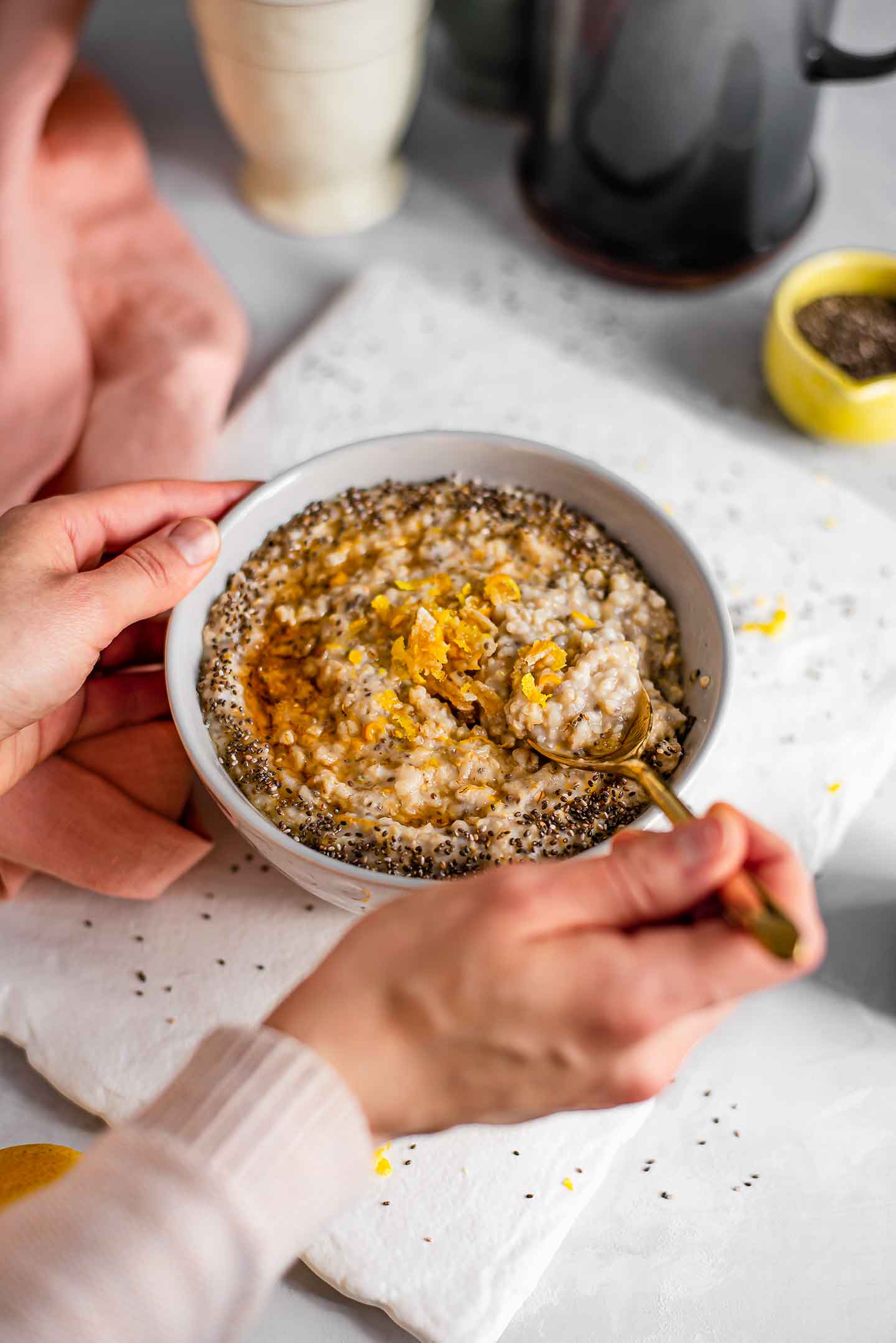 Side view of a hand scooping a spoonful of lemon chia oatmeal topped with lemon zest, chia seeds, and maple syrup.