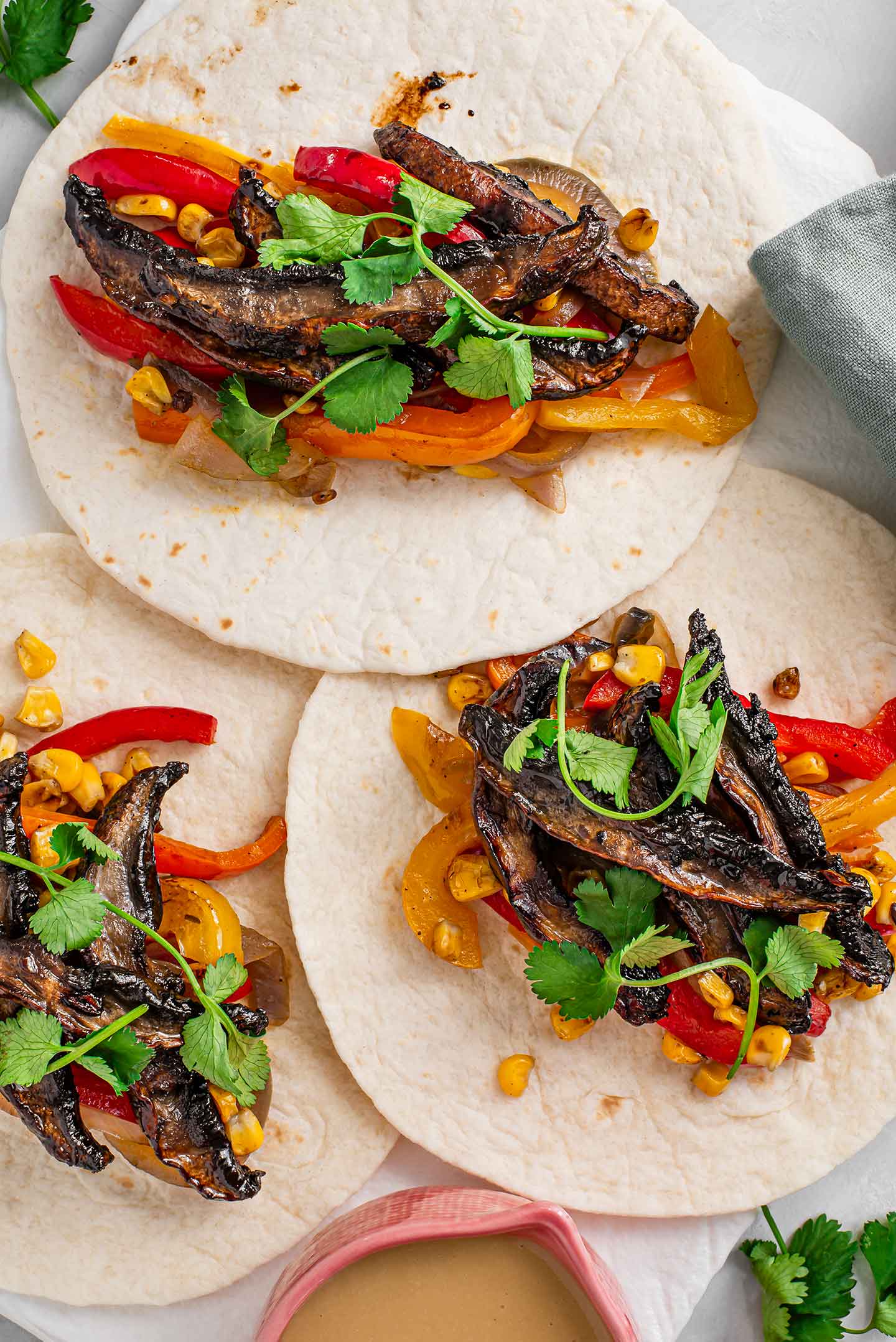 Top down view of three spicy and sweet sesame fajitas on a tray with charred corn, grilled bell peppers and red onion, and topped with cilantro.