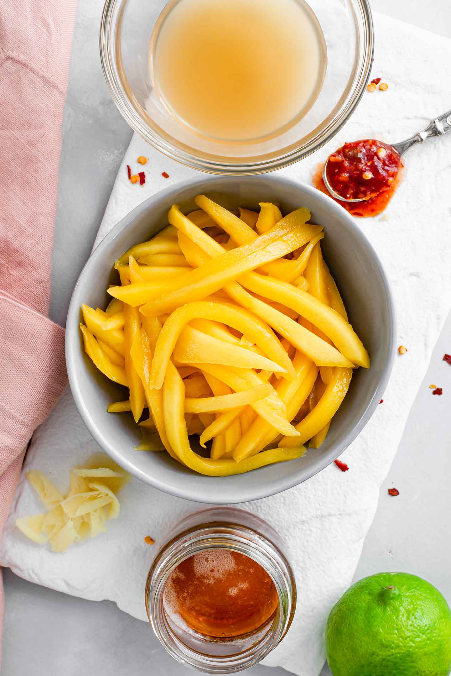 Top down view of sliced mango in a small dish surrounded by apple cider vinegar, chilli garlic sauce, fresh ginger, maple syrup, and a lime.