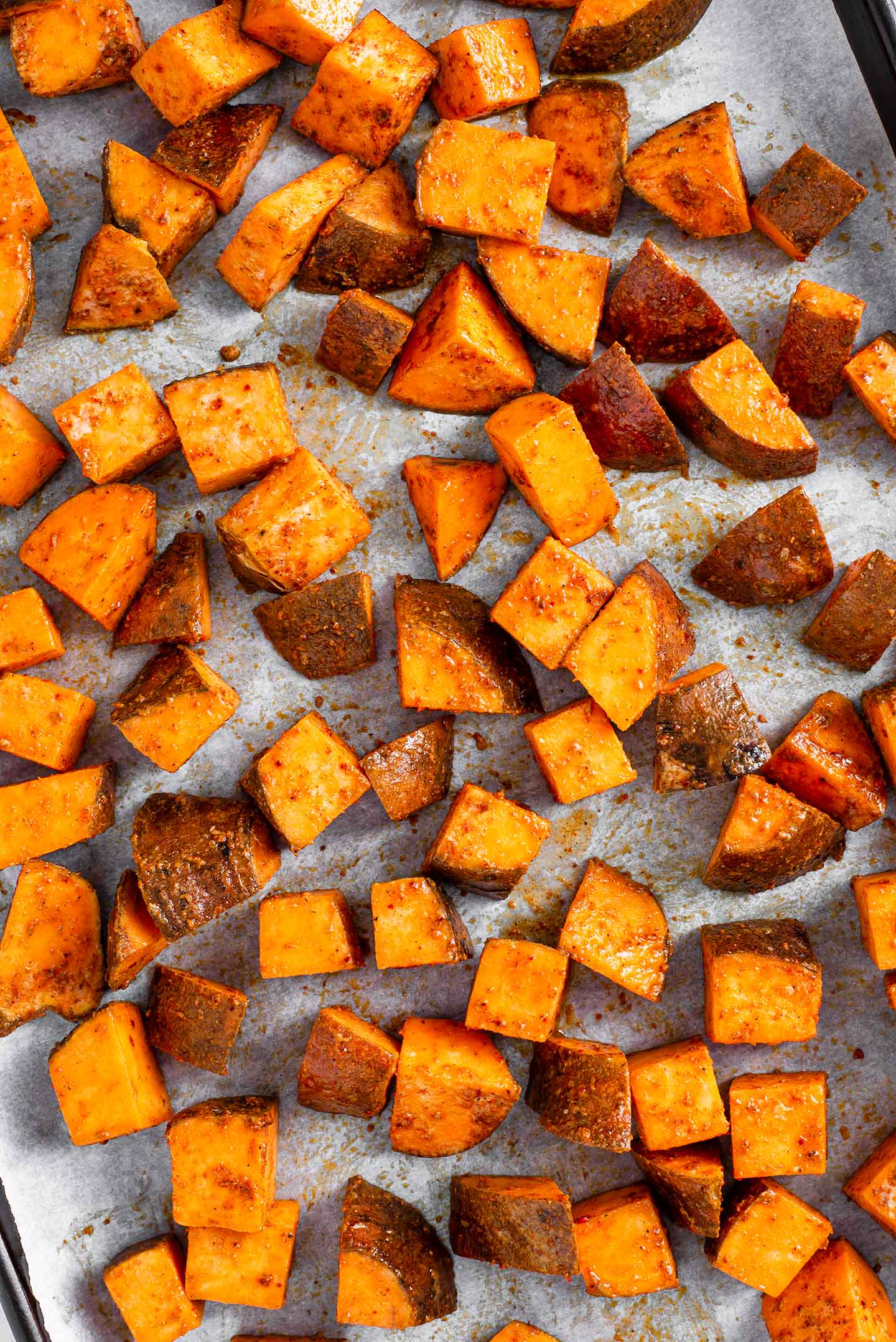 Top down view of sweet potato cubes scattered on a parchment lined baking tray.