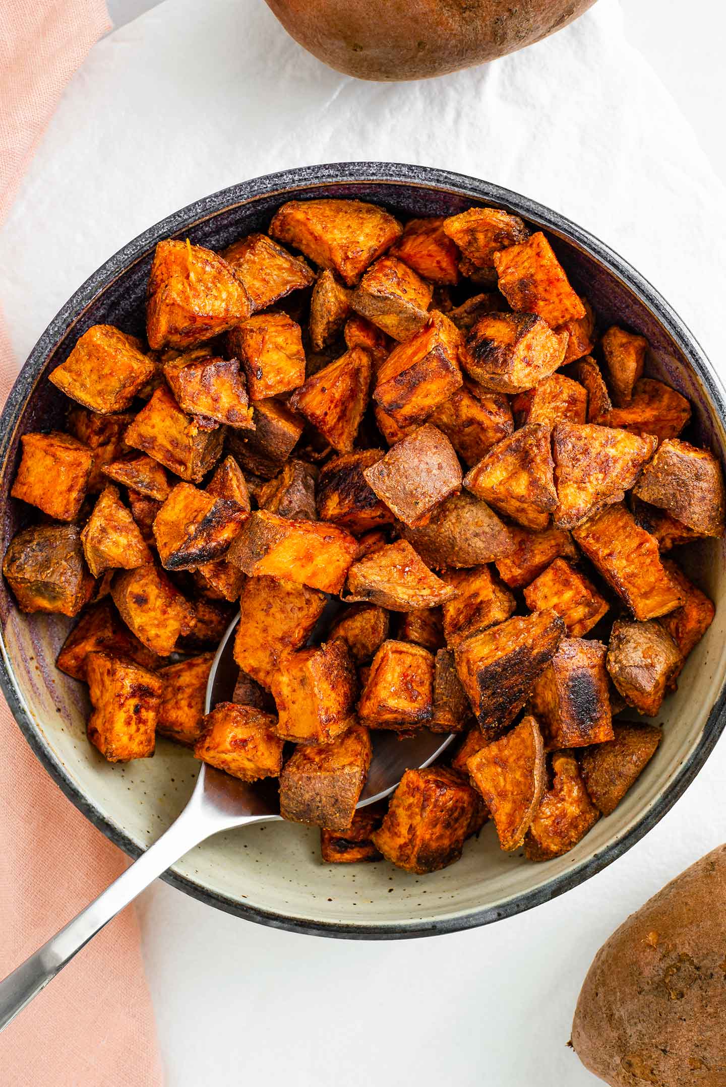 Top down view of crispy cubed sweet potato filling a shallow bowl with a serving spoon.