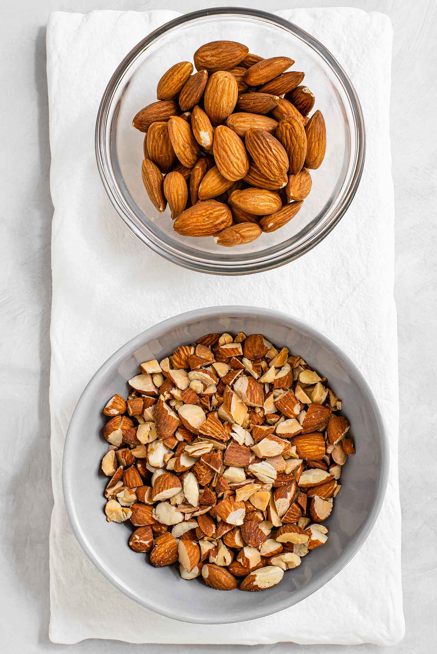 Top down view of two small dishes. In one dish are whole almonds and in the other dish, the almonds are coarsely chopped and lightly browned from being roasted.