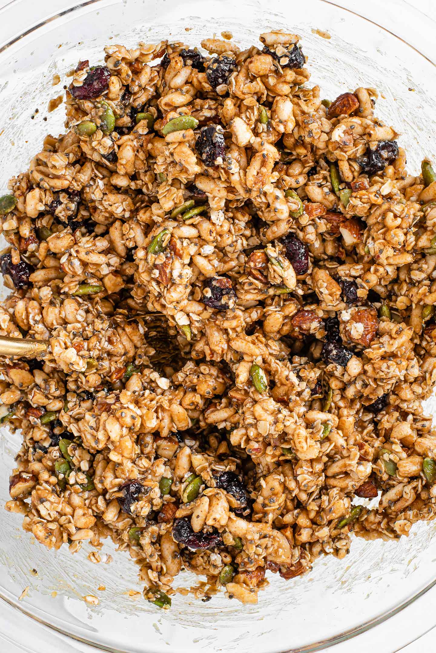 Top down view of the puffed granola bar mixture combined in a large glass bowl. The mixture is sticky and fully coated.