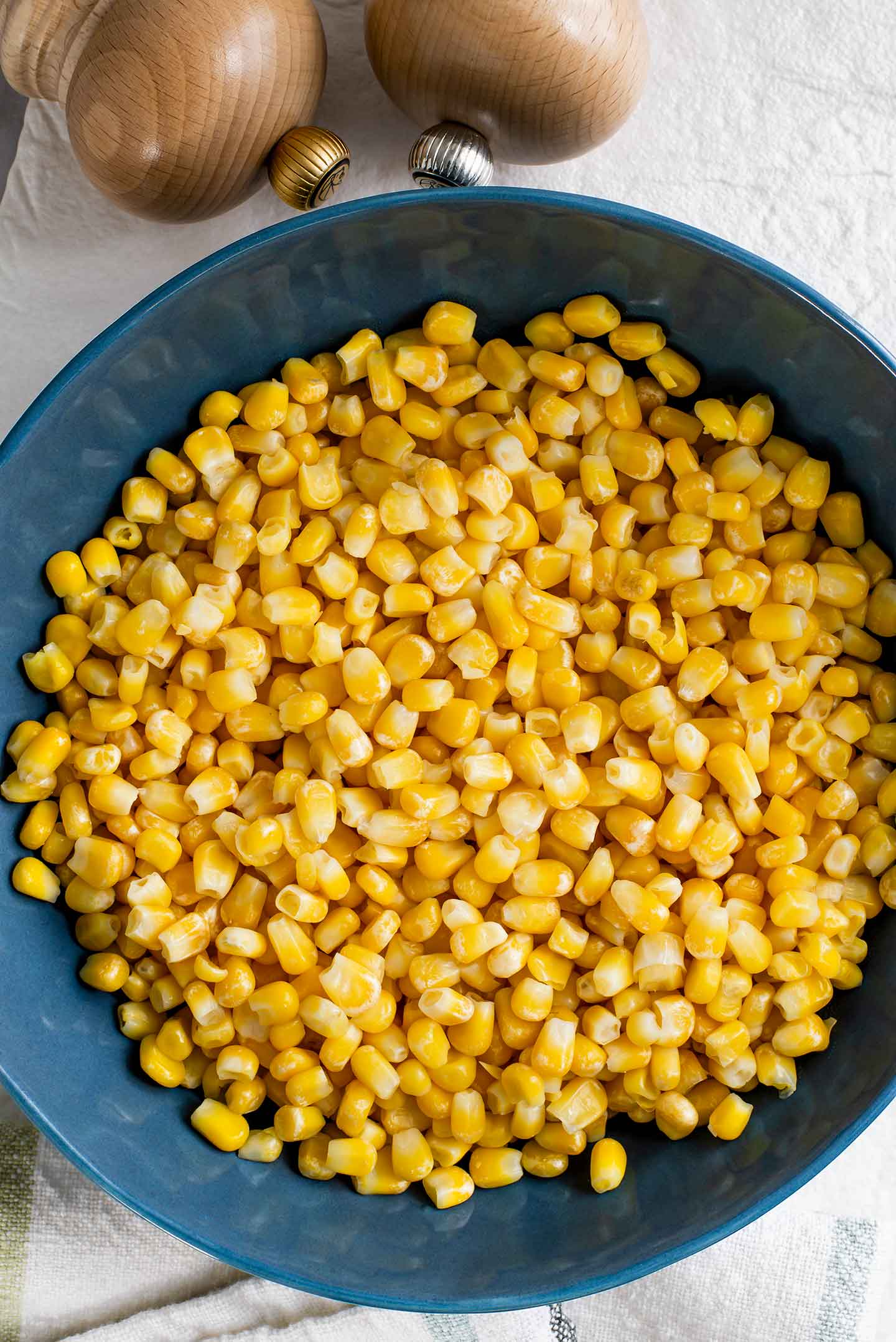 Top down view of yellow corn kernels in a serving bowl before being charred in the skillet. Salt and pepper shakers lay beside the bowl.