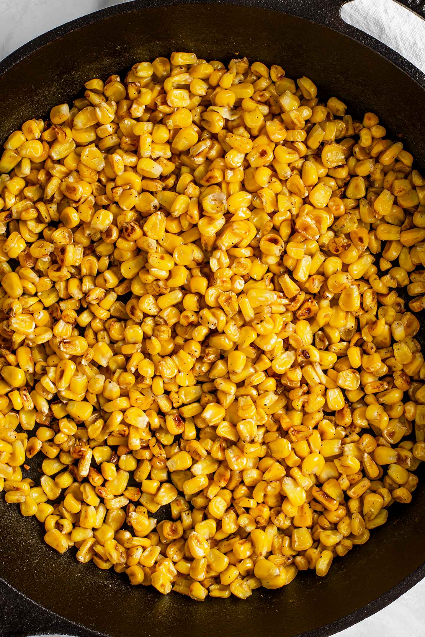 Top down view of blackened, charred corn in a cast iron skillet. The kernels are golden and darkened with browned bits.