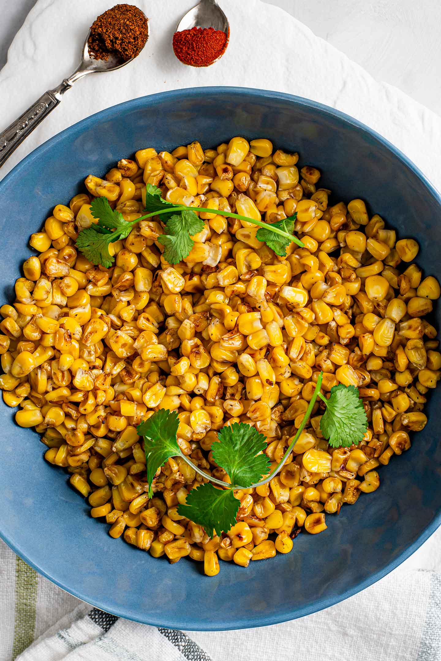 Top down view of skillet charred corn in a blue serving bowl. Sprigs of cilantro sit atop the deep yellow, browned corn kernels.