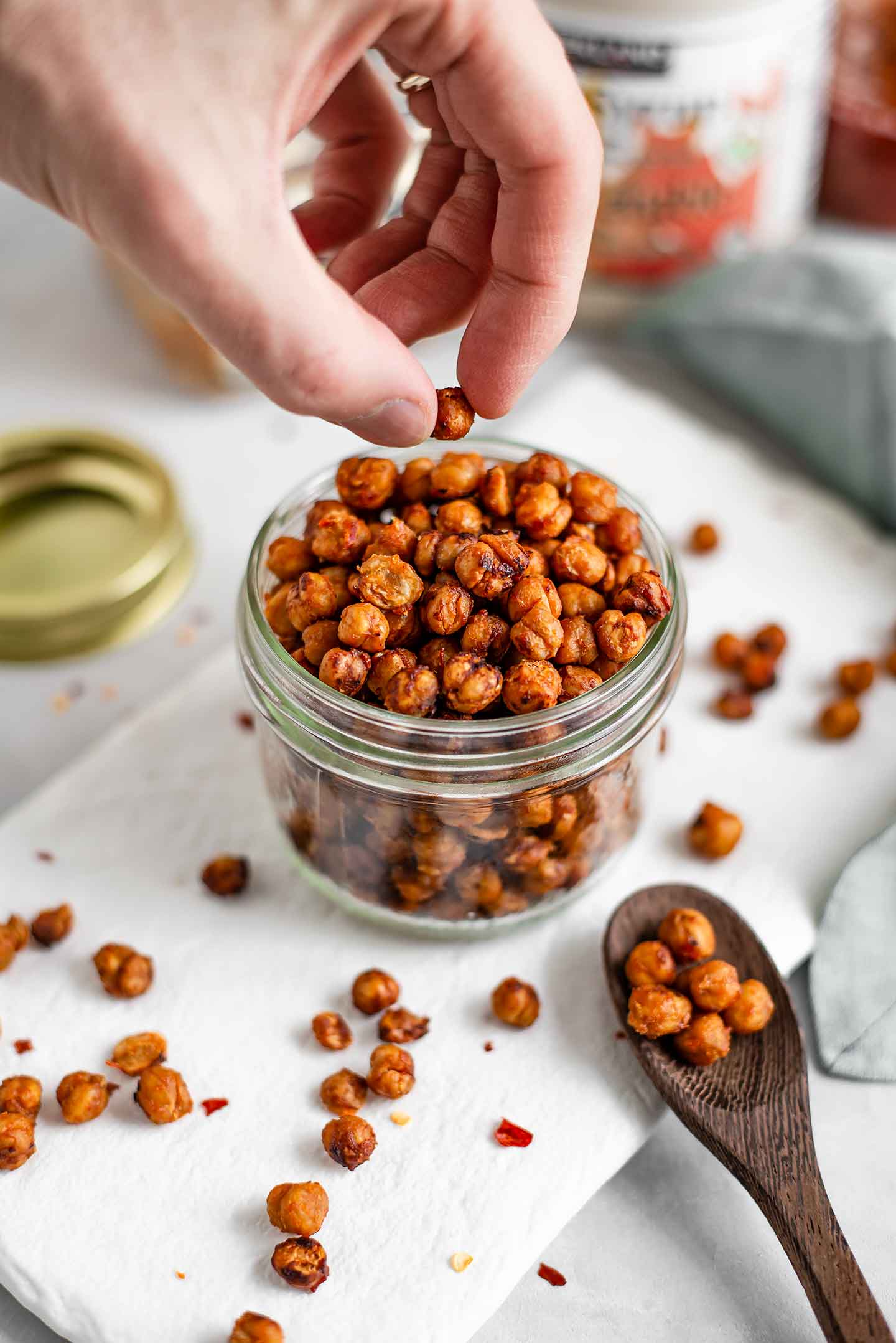 Side view of hand picking up a roasted chickpea from a jar of the tasty snack.