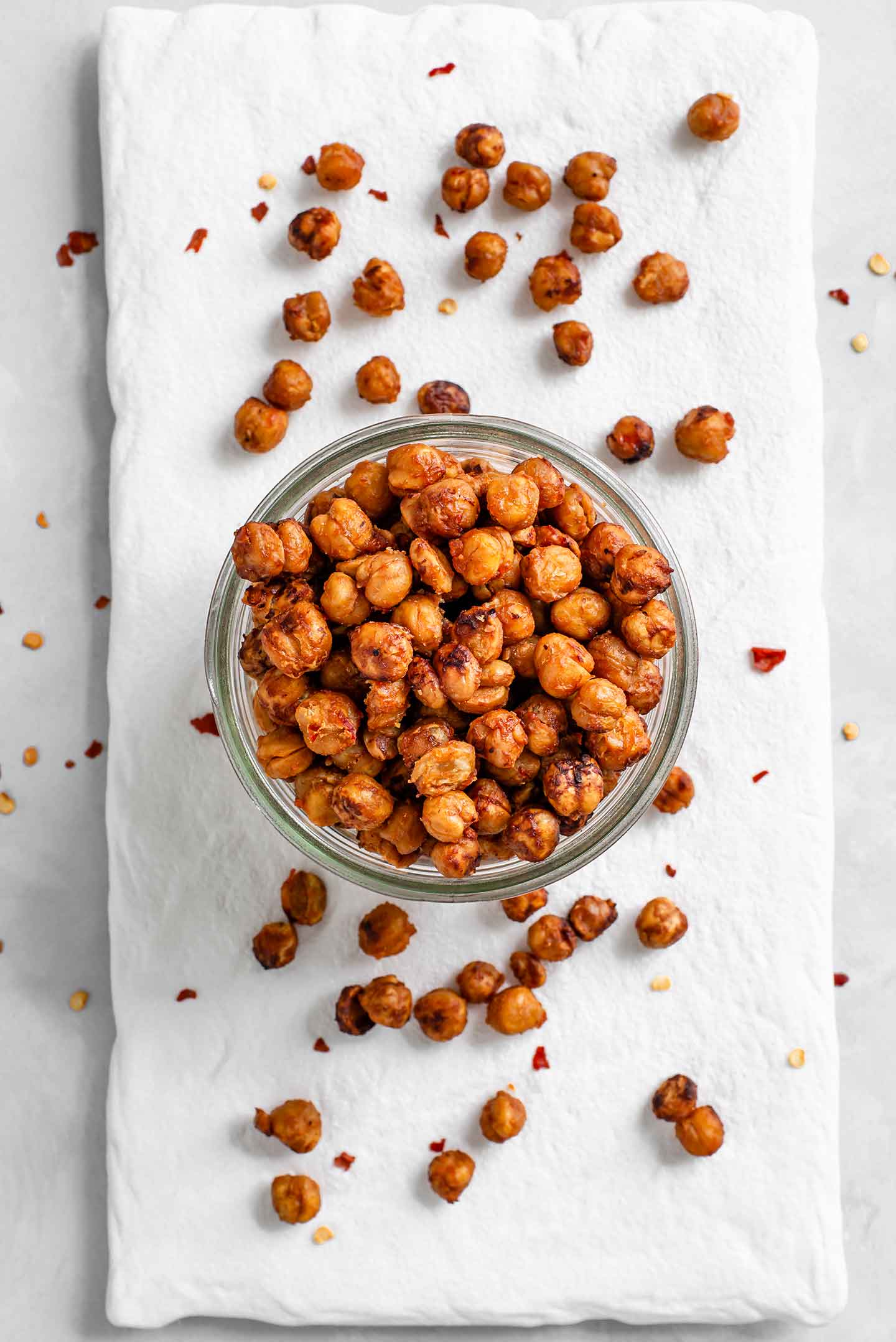 Top down view of chilli miso roasted chickpeas in a glass jar. Roasted chickpeas are scattered around the jar on a white tray.