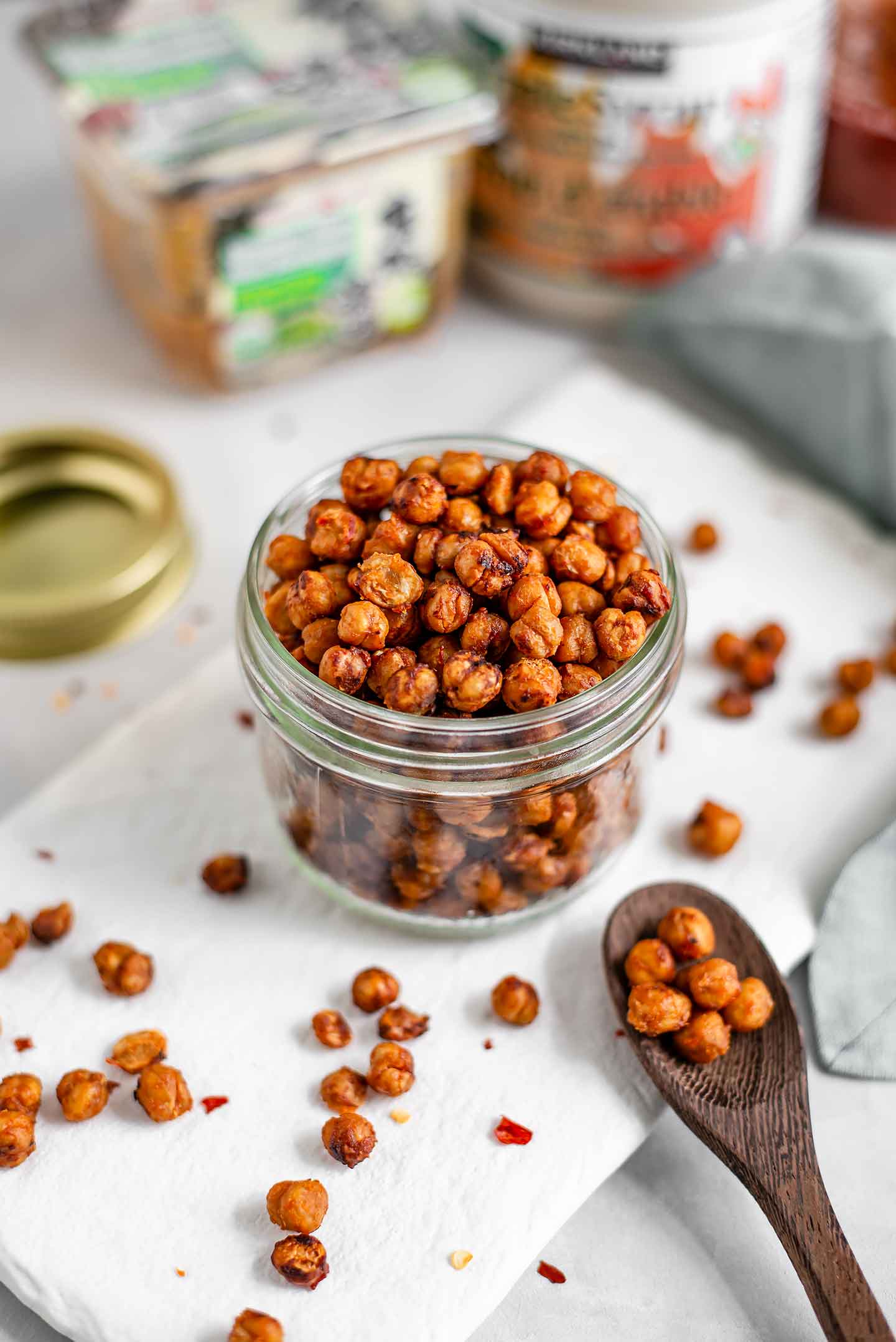 Side view of roasted chickpeas in a glass jar. Miso paste, chilli garlic sauce, and maple syrup are in the background.
