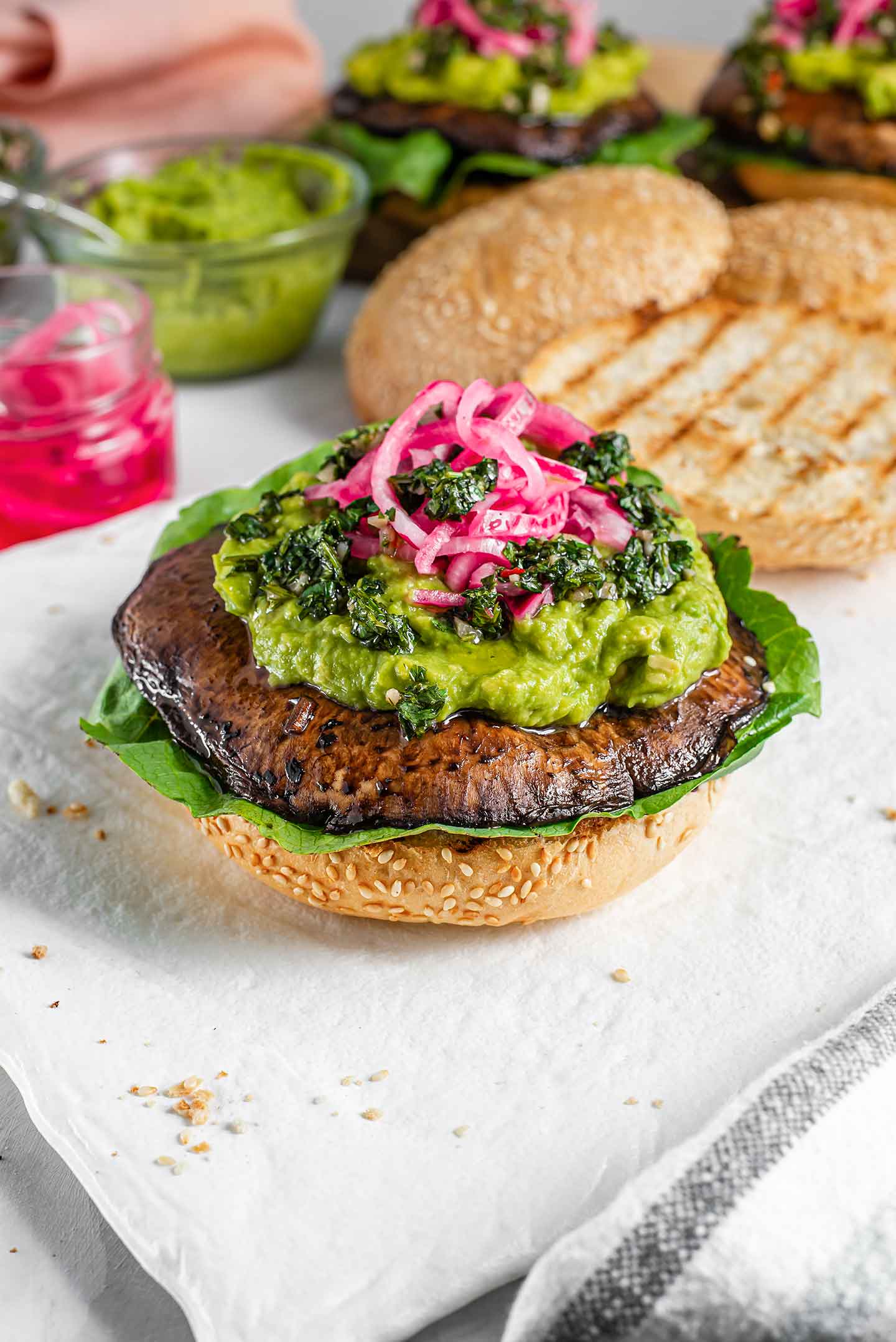 Top down view of a burger without the top bun. Romaine lettuce lays under the mushroom patty with avocado, chimichurri, and pickled red onion on top.