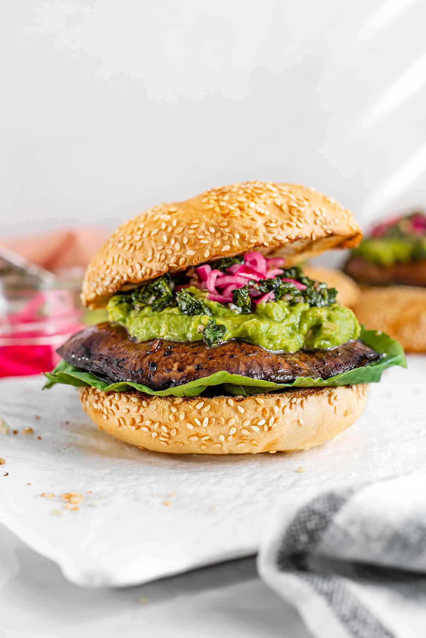 Side view of a burger with romaine lettuce, a portobello mushroom, a generous amount of avocado mash and topped with chimichurri and pickled red onion.