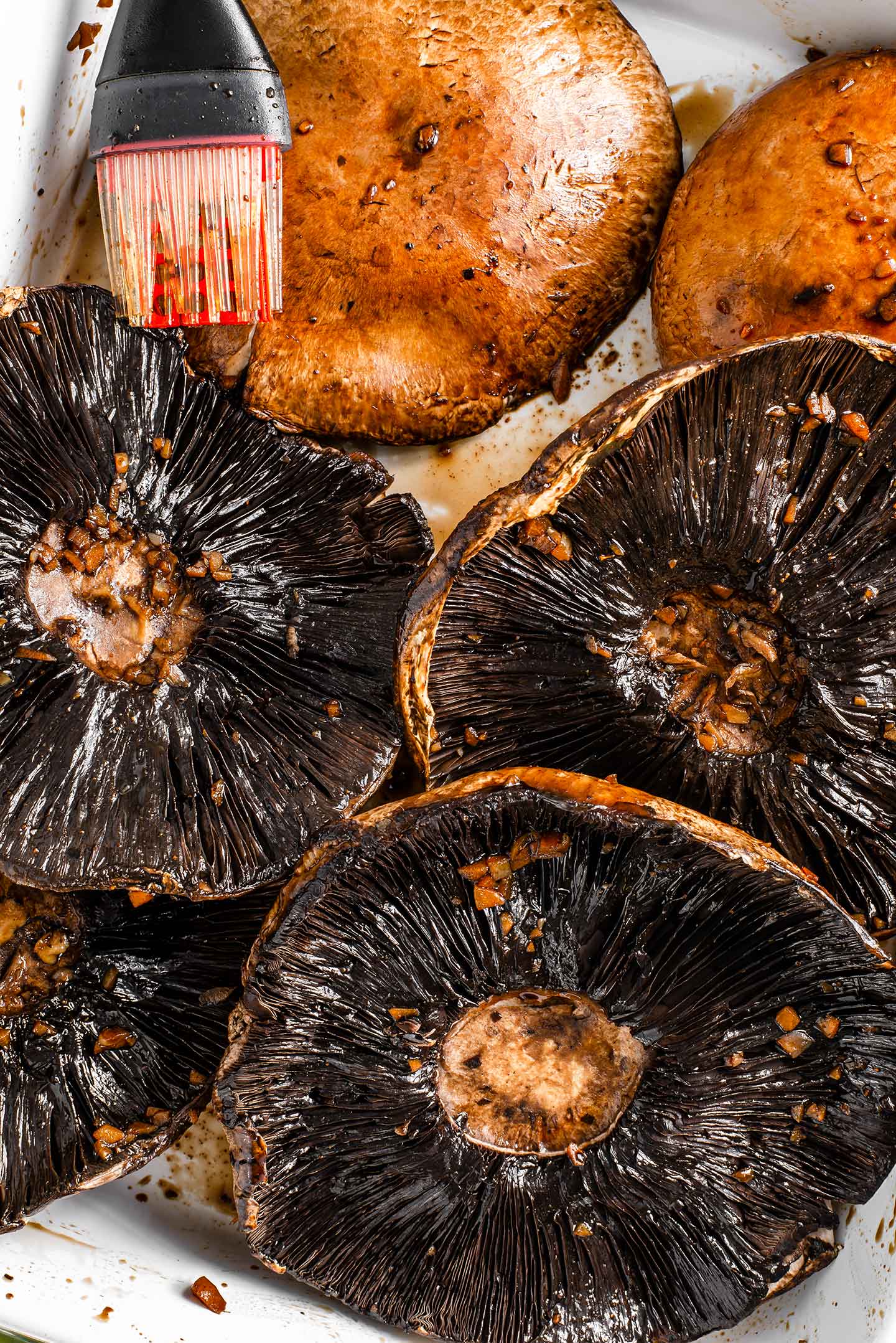 Top down view of portobello mushrooms being brushed with marinade in a large dish.