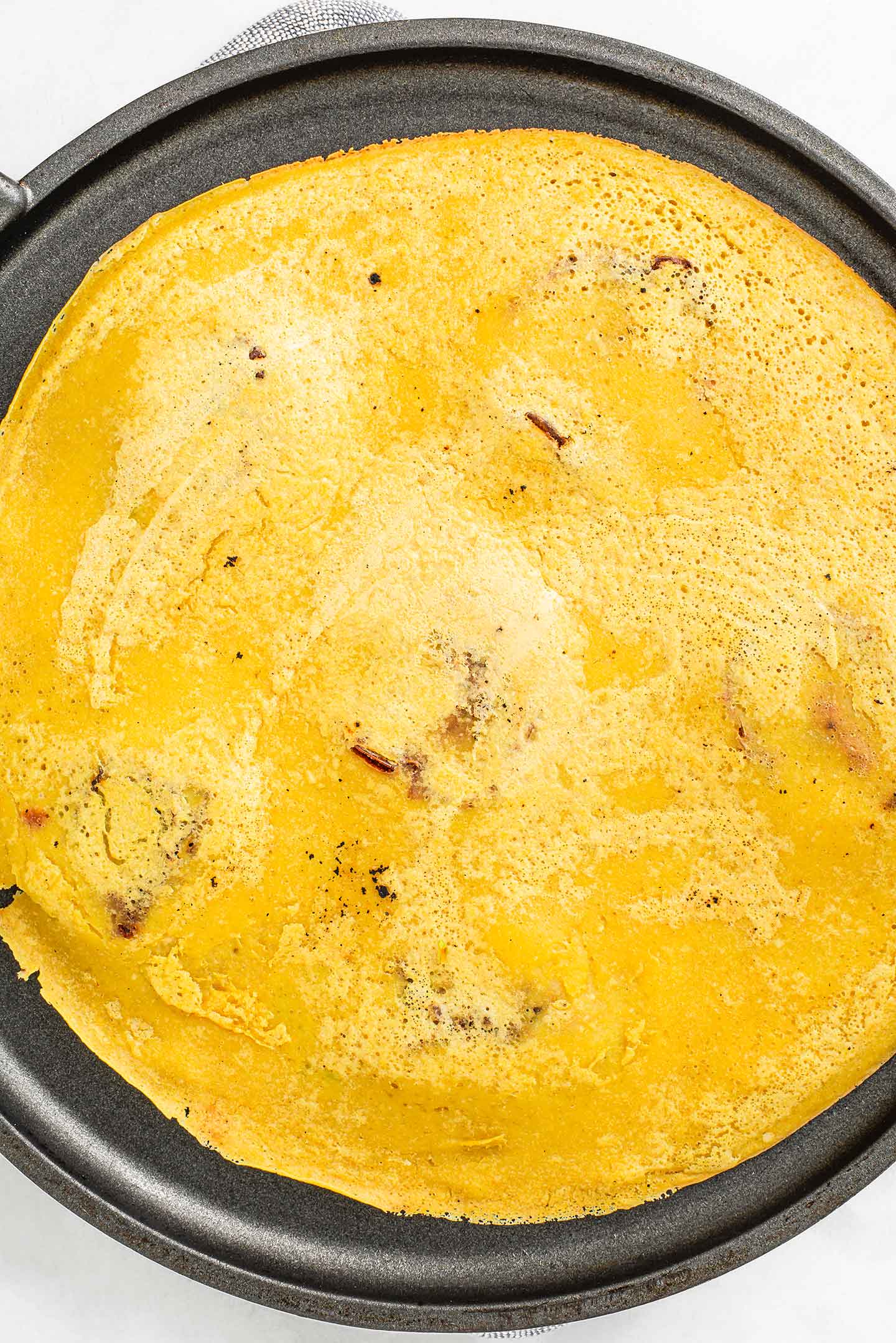 Top down view of a golden chickpea omelette flipped on a non-stick skillet so the top can cook.