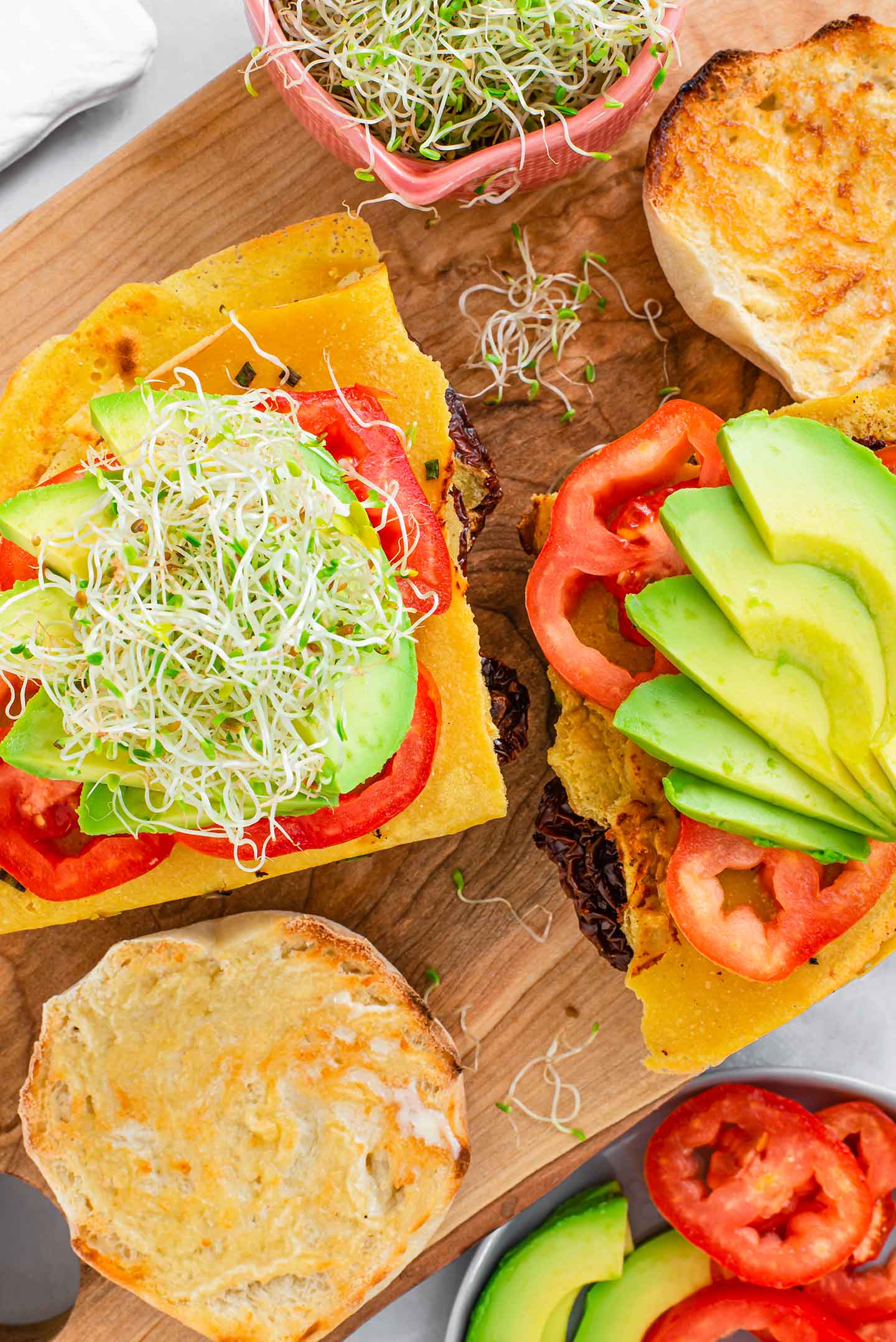 Top down view of two vegan Portuguese breakfast sandwiches without the tops. The omelettes have been folded into a triangular shape to fit on the sweet muffin bun.