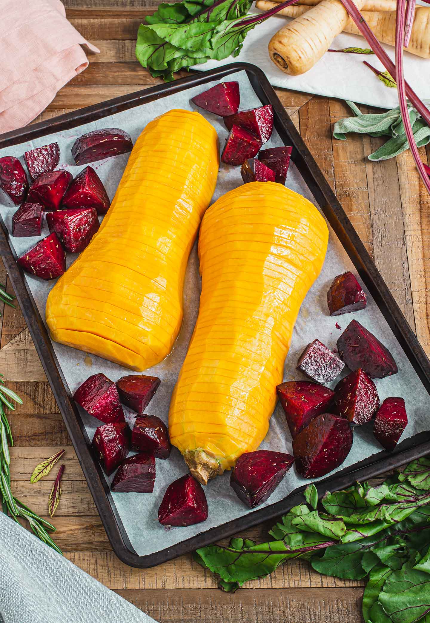 Top down view of hasselback butternut squash and raw beets on a baking tray lined with parchment paper.